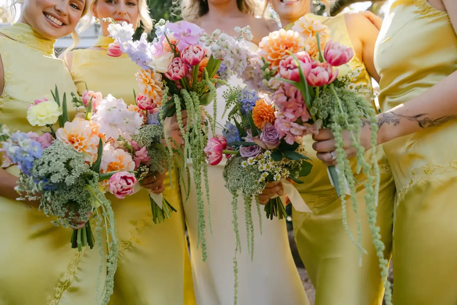 A group of women in yellow dresses holding colorful flower bouquets at an outdoor event.