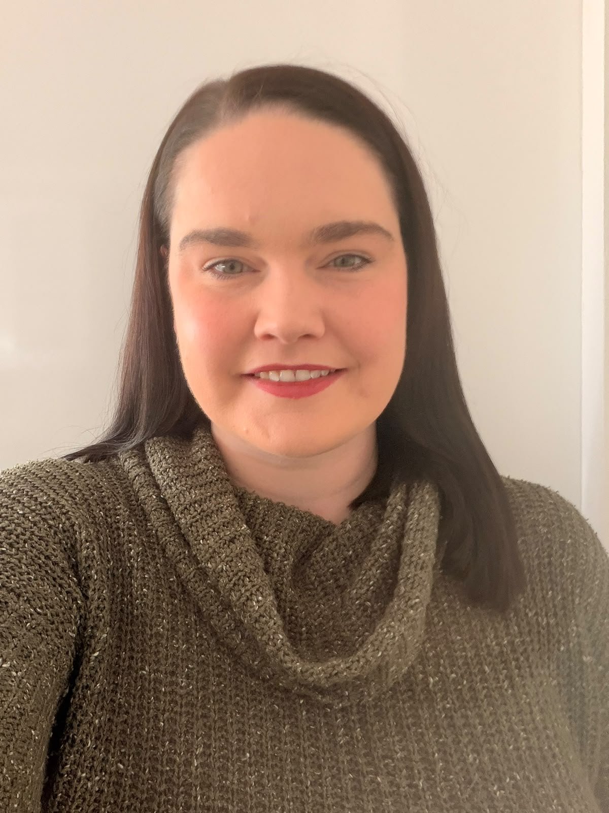 Smiling woman with long dark hair wearing a chunky brown knit sweater in a close-up portrait