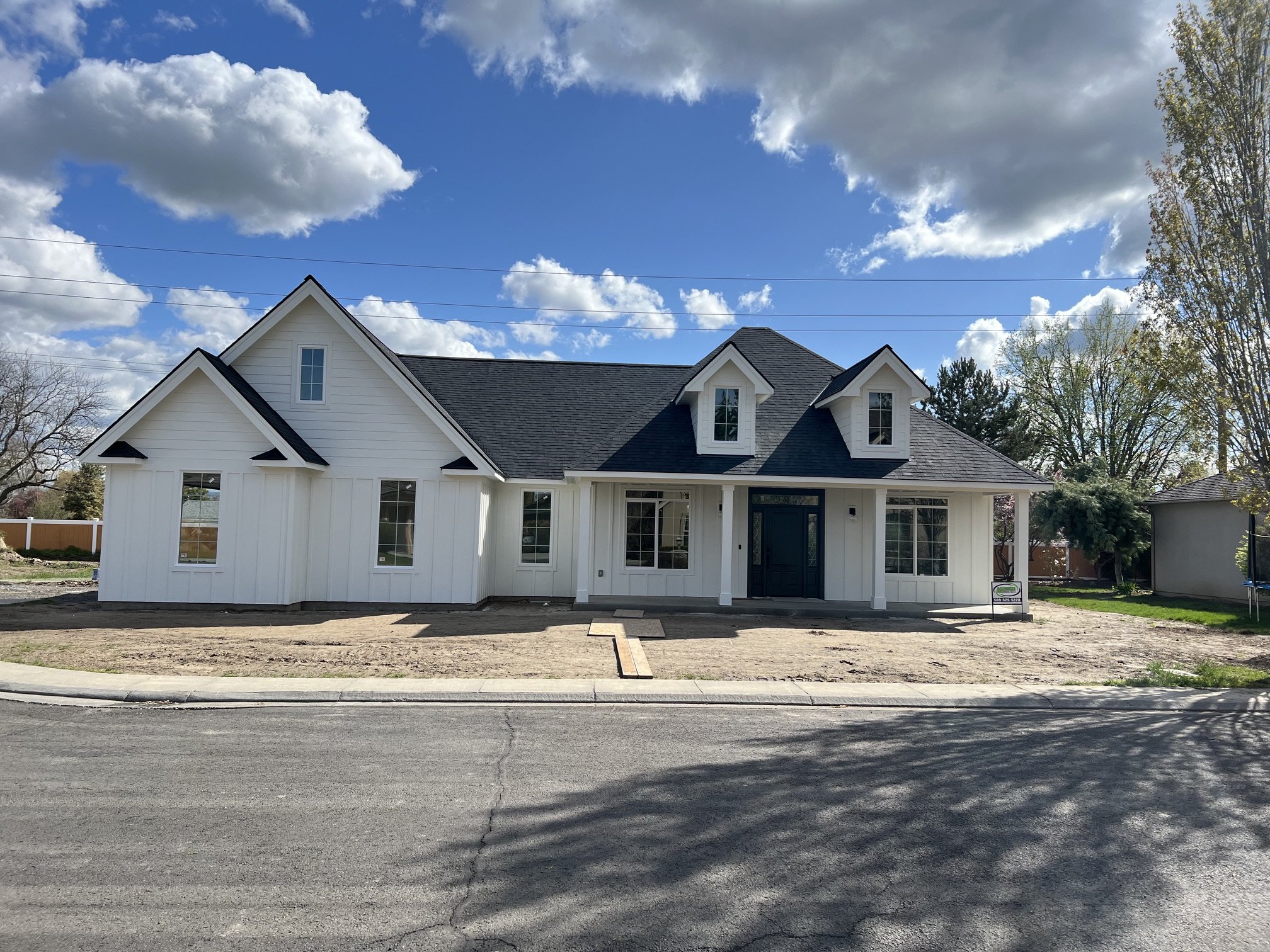 New white two-story house with black roof, multiple windows, front porch, and landscaping, under a partly cloudy blue sky.