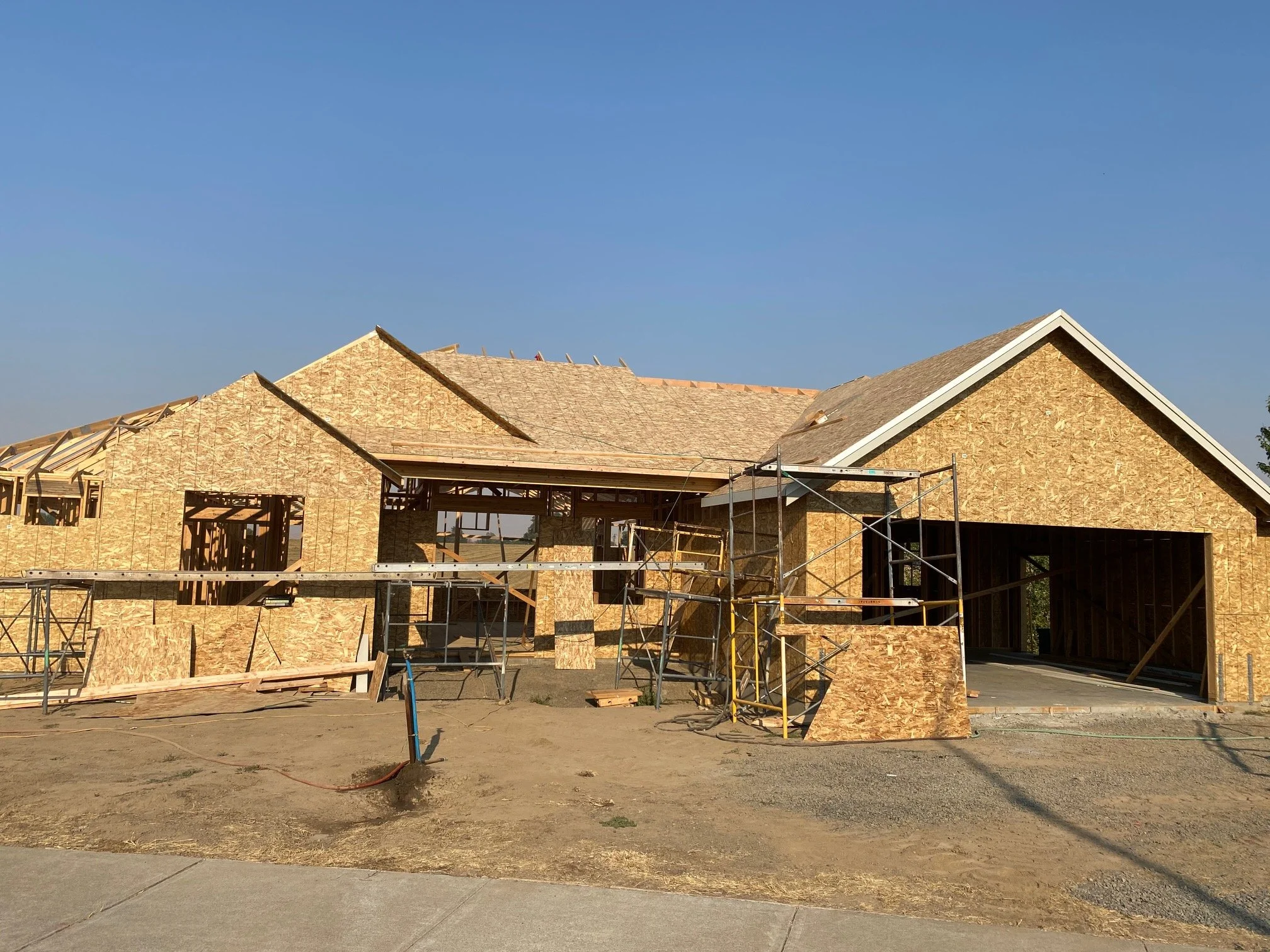 A house under construction with wooden framing and scaffolding, set against a clear blue sky.