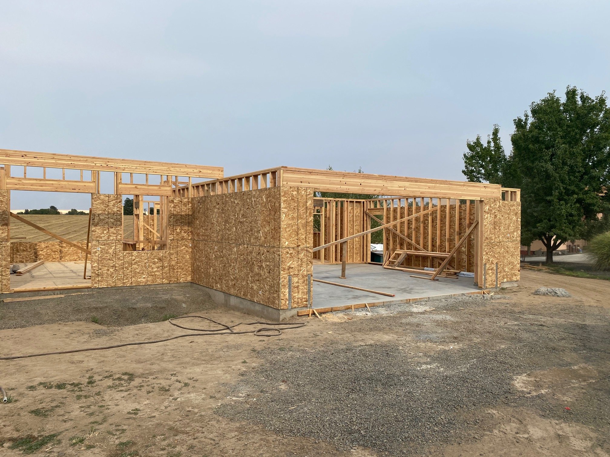 Construction site with wooden framing for a building, open roof structure, and partially finished walls. Trees and overcast sky in the background.