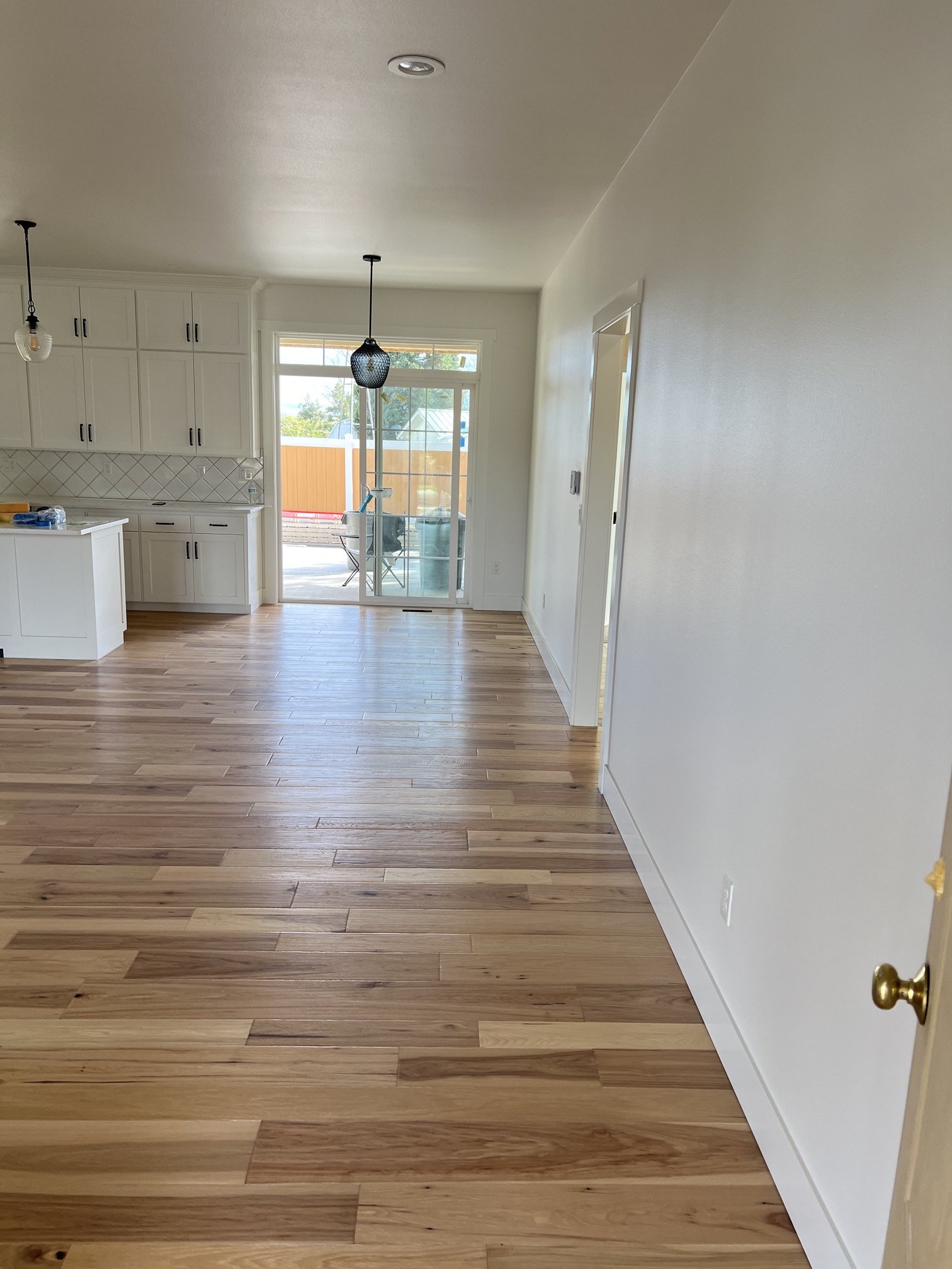 Interior view of a room with hardwood floors, white cabinetry, and a sliding glass door leading outside, with two pendant lights hanging from the ceiling.
