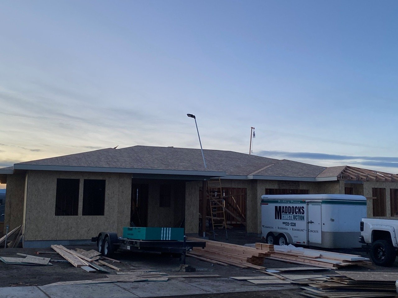 Under construction house with a trailer and construction materials outside during dusk.