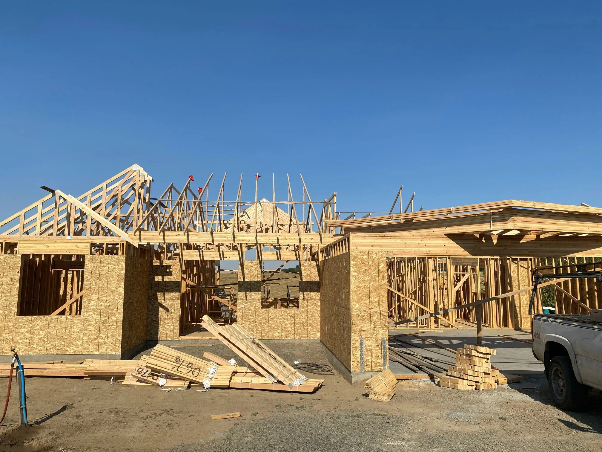 The construction site shows a building under construction with wooden framing and plywood walls, against a clear blue sky.