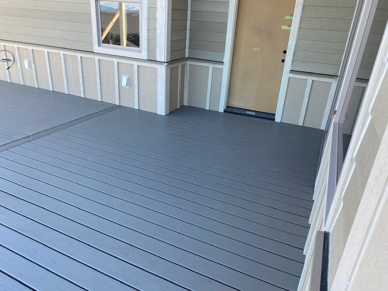 Newly installed gray wooden deck outside a house with siding, window, and door.