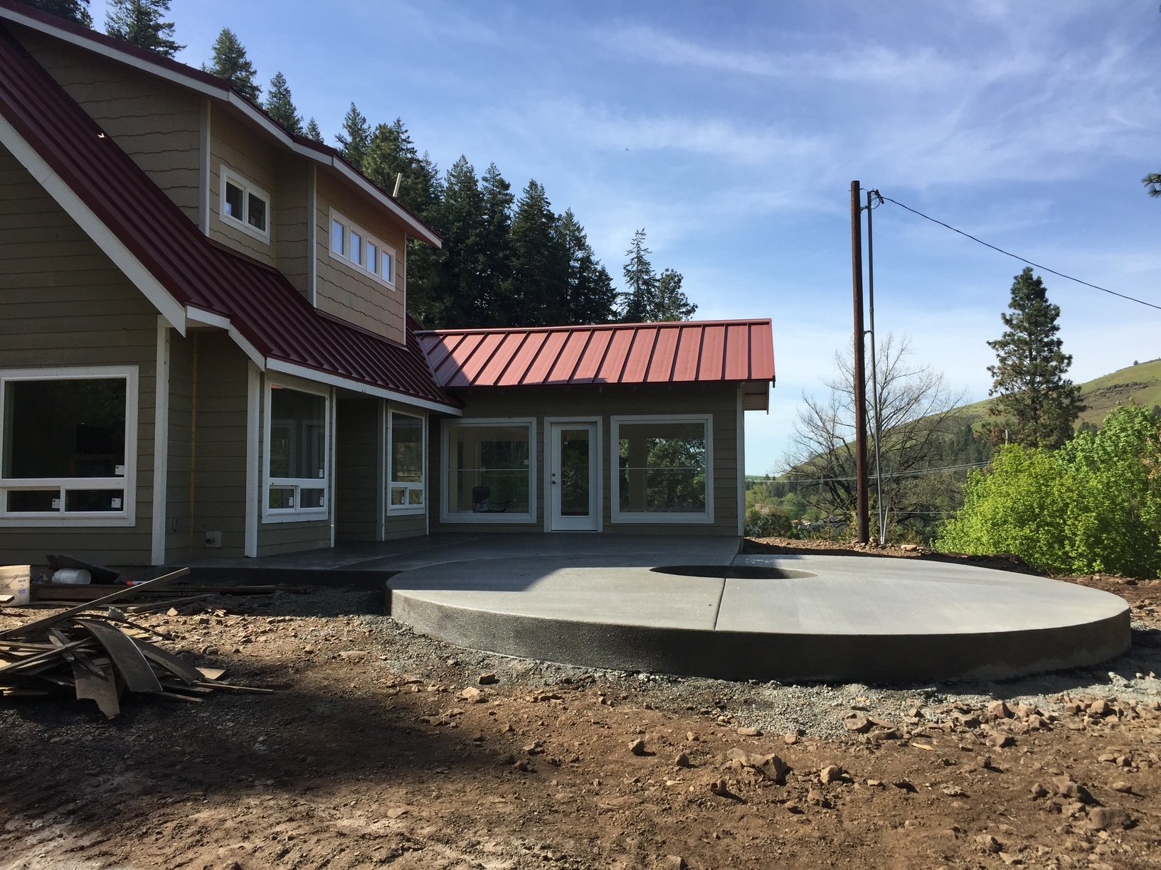 Newly constructed house with a dirt yard, a concrete patio, and a landscape of green trees and hills.