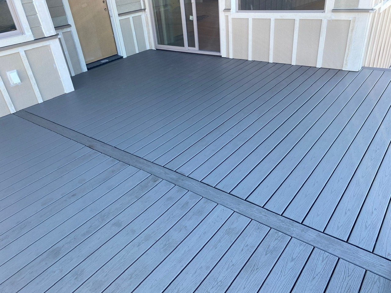 A newly constructed outdoor deck made of gray composite decking boards with a sliding glass door leading into the house.