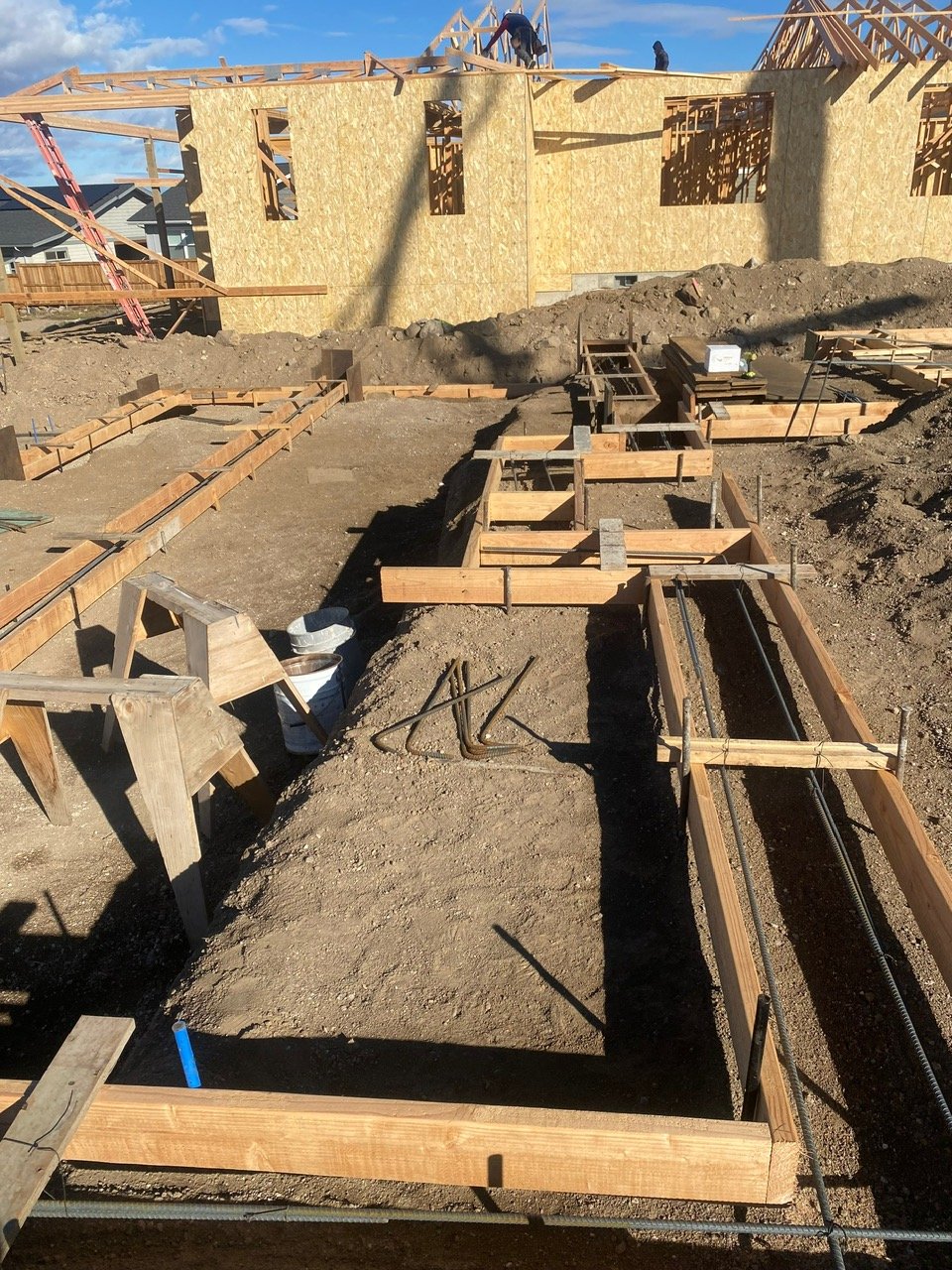 Construction site with wooden framing for building foundation and an unfinished house in the background.