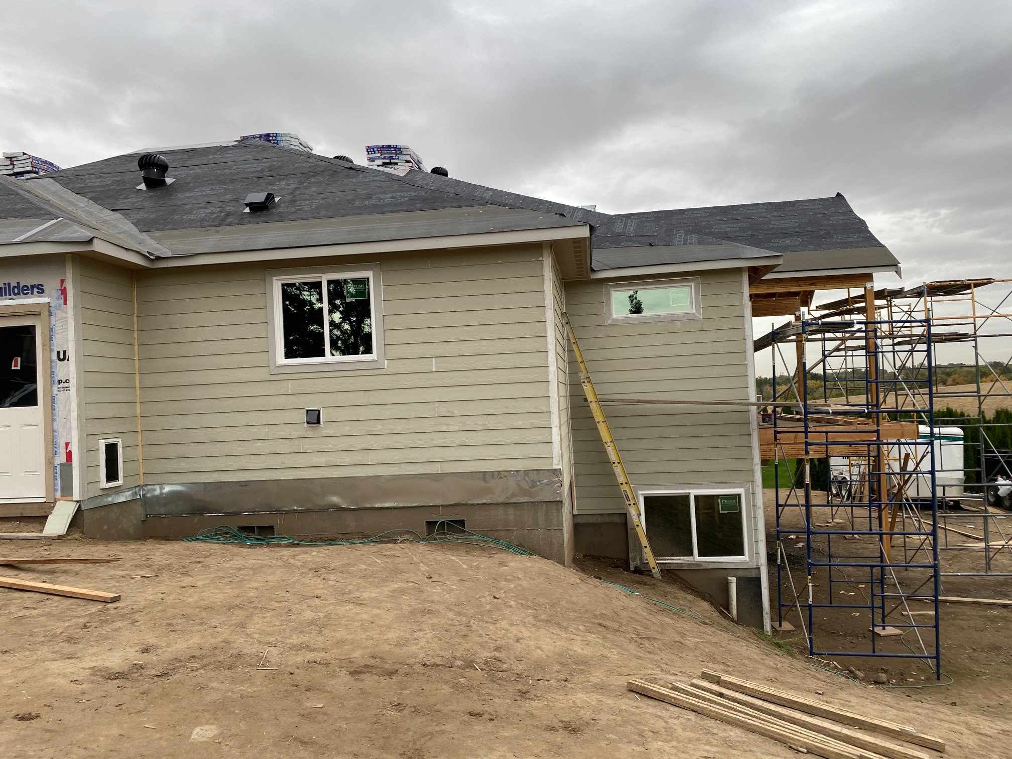 House under construction with scaffolding and roofing in progress, overcast sky