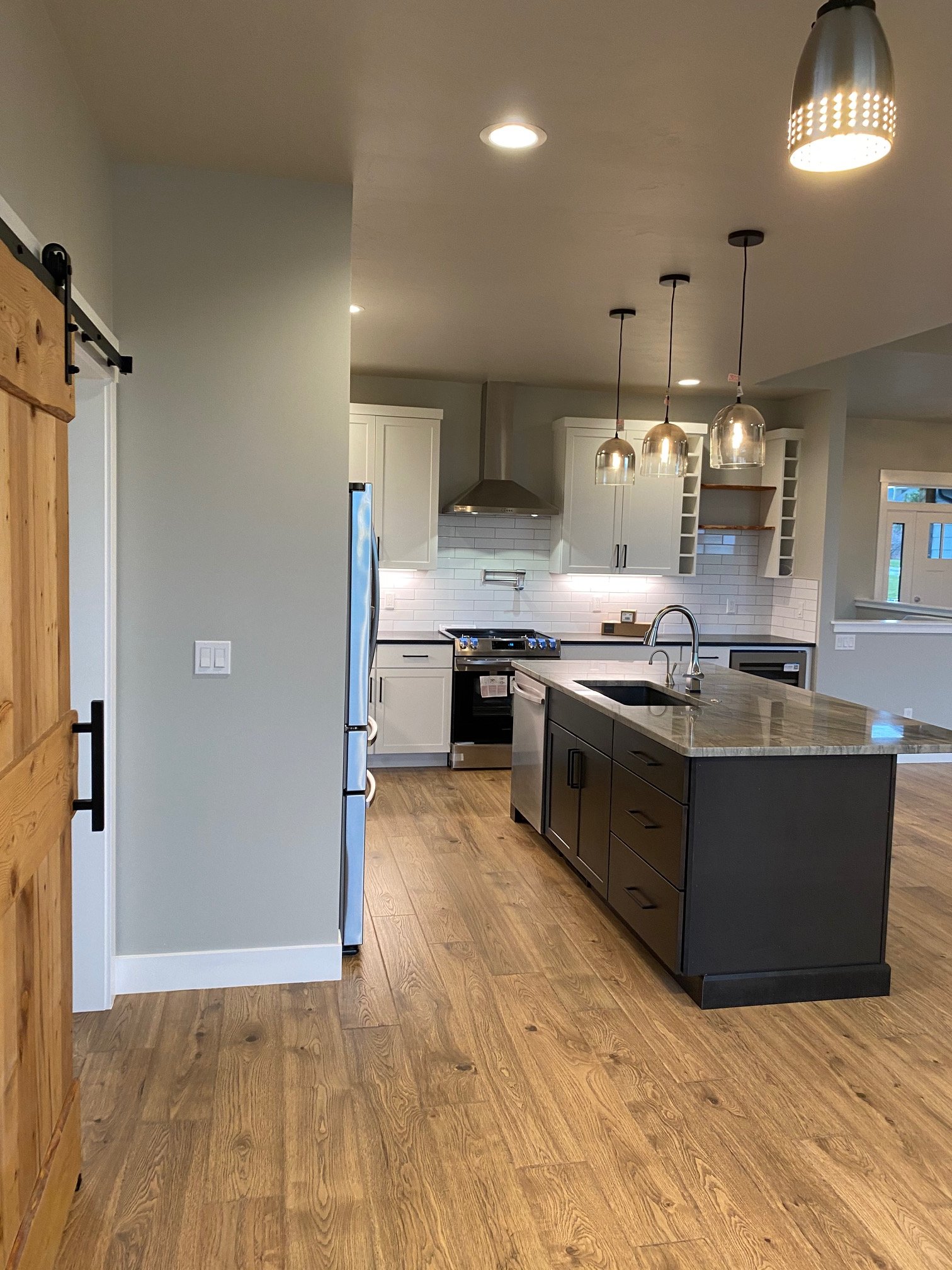 Modern kitchen with white cabinets, stainless steel stove and range hood, central island with a granite countertop, pendant lights, and hardwood flooring.