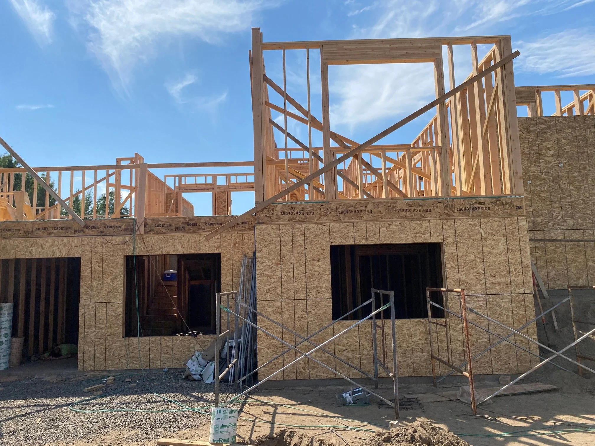 Wood framing structure of a two-story building under construction with blue sky and clouds in the background.