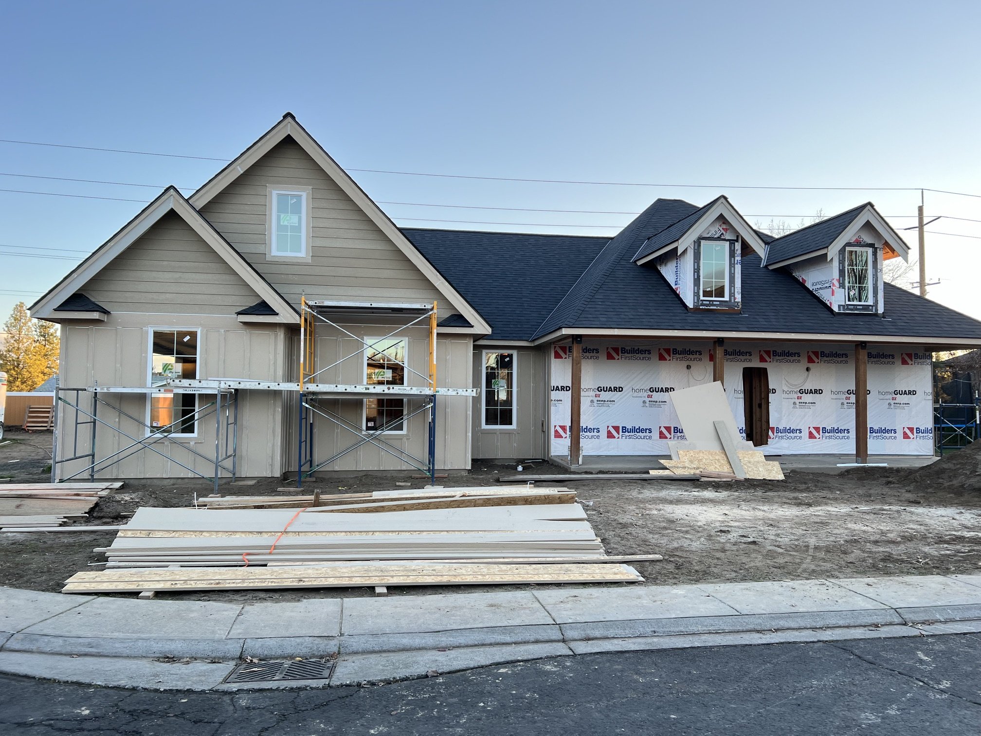 House under construction with scaffolding on the front, two dormer windows on the roof, and building materials on the ground.