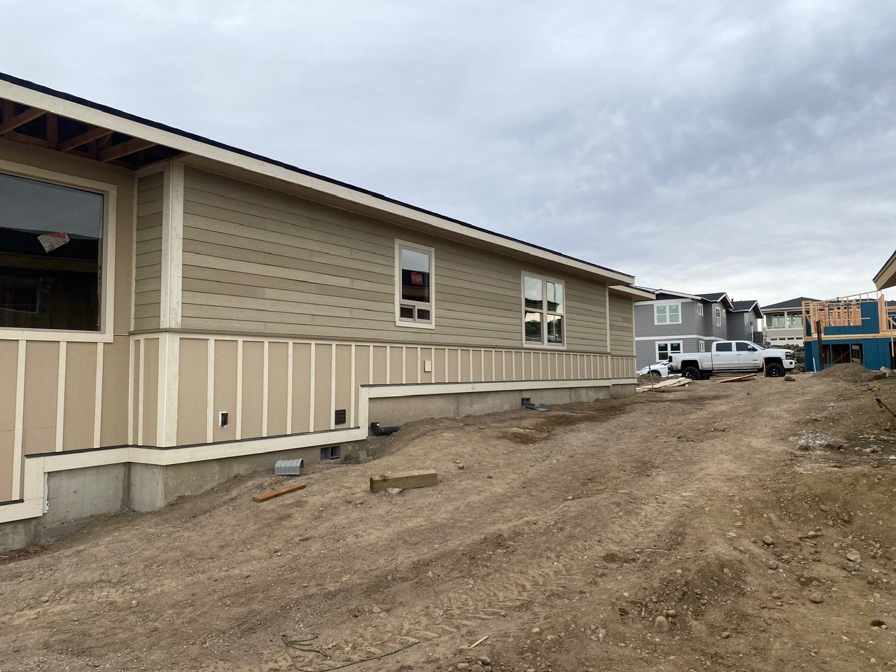 Newly constructed house with beige siding and three windows, surrounded by dirt and construction materials.