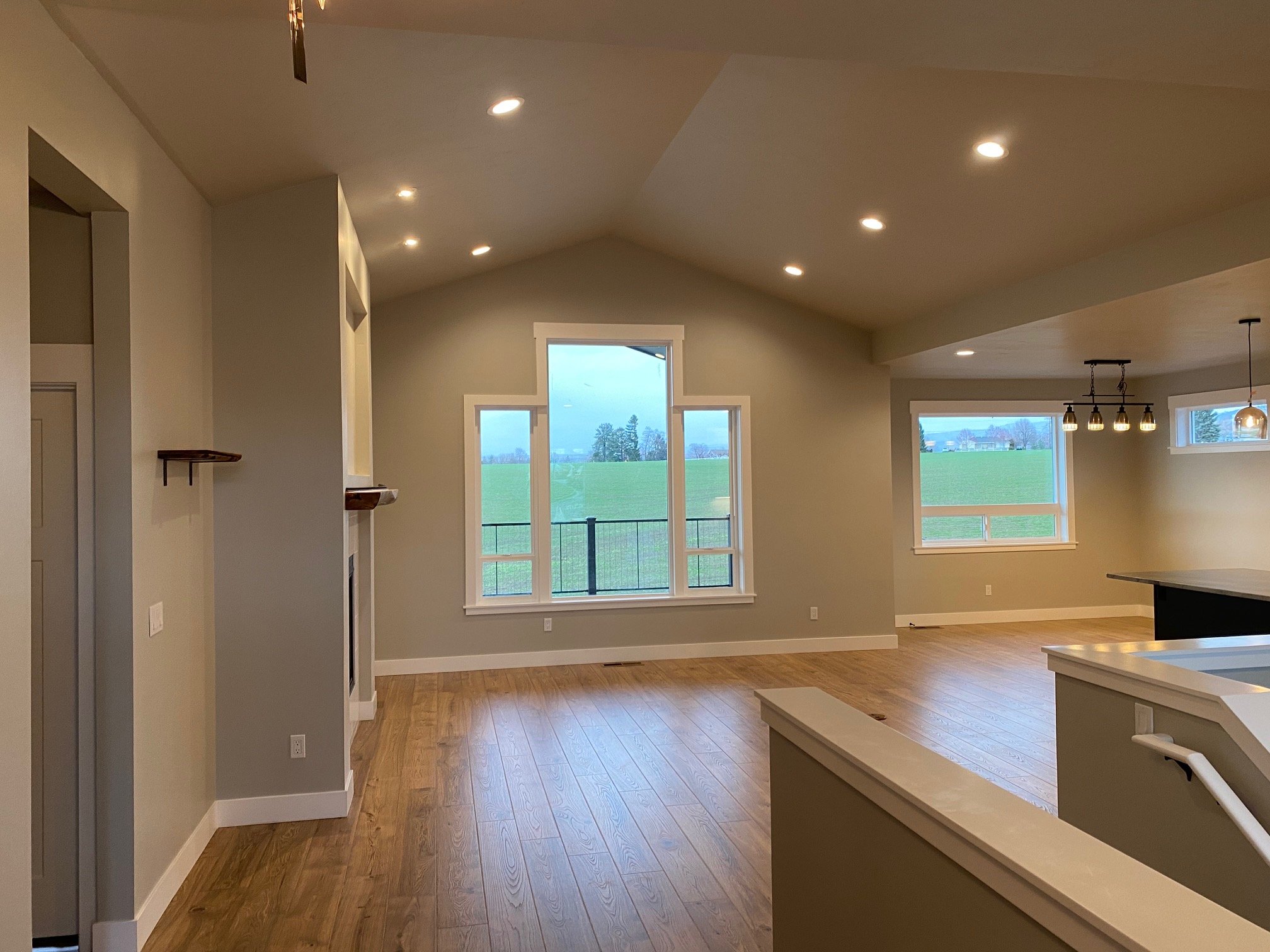 Interior of a modern home with large windows, hardwood floors, recessed ceiling lights, and a view of a green field outside.