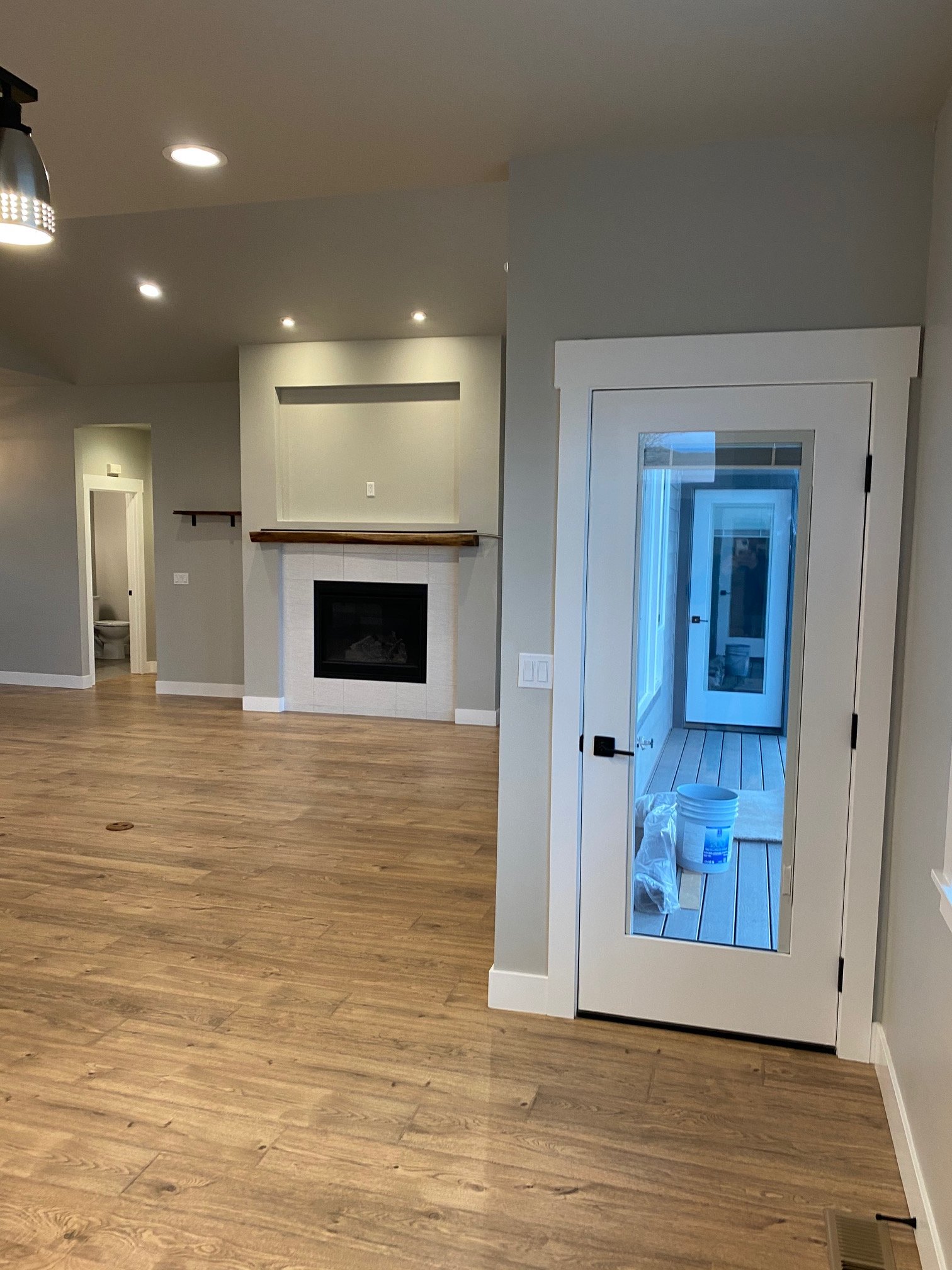 Living room area with wood flooring, a fireplace, and an enclosed porch with a door that has glass panels. There is a small bathroom or closet opening to the left and recessed lighting in the ceiling.