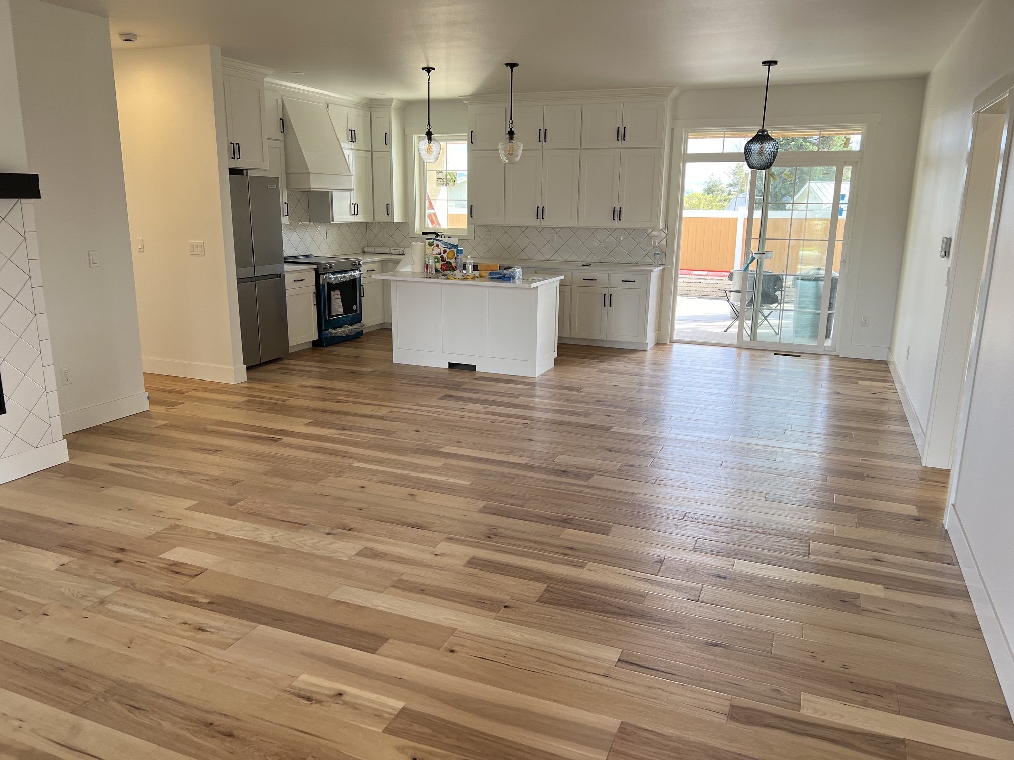 A spacious, modern kitchen with white cabinets, stainless steel appliances, a small central island, and hardwood floors. There's a sliding glass door leading outside, with a patio and outdoor furniture visible.