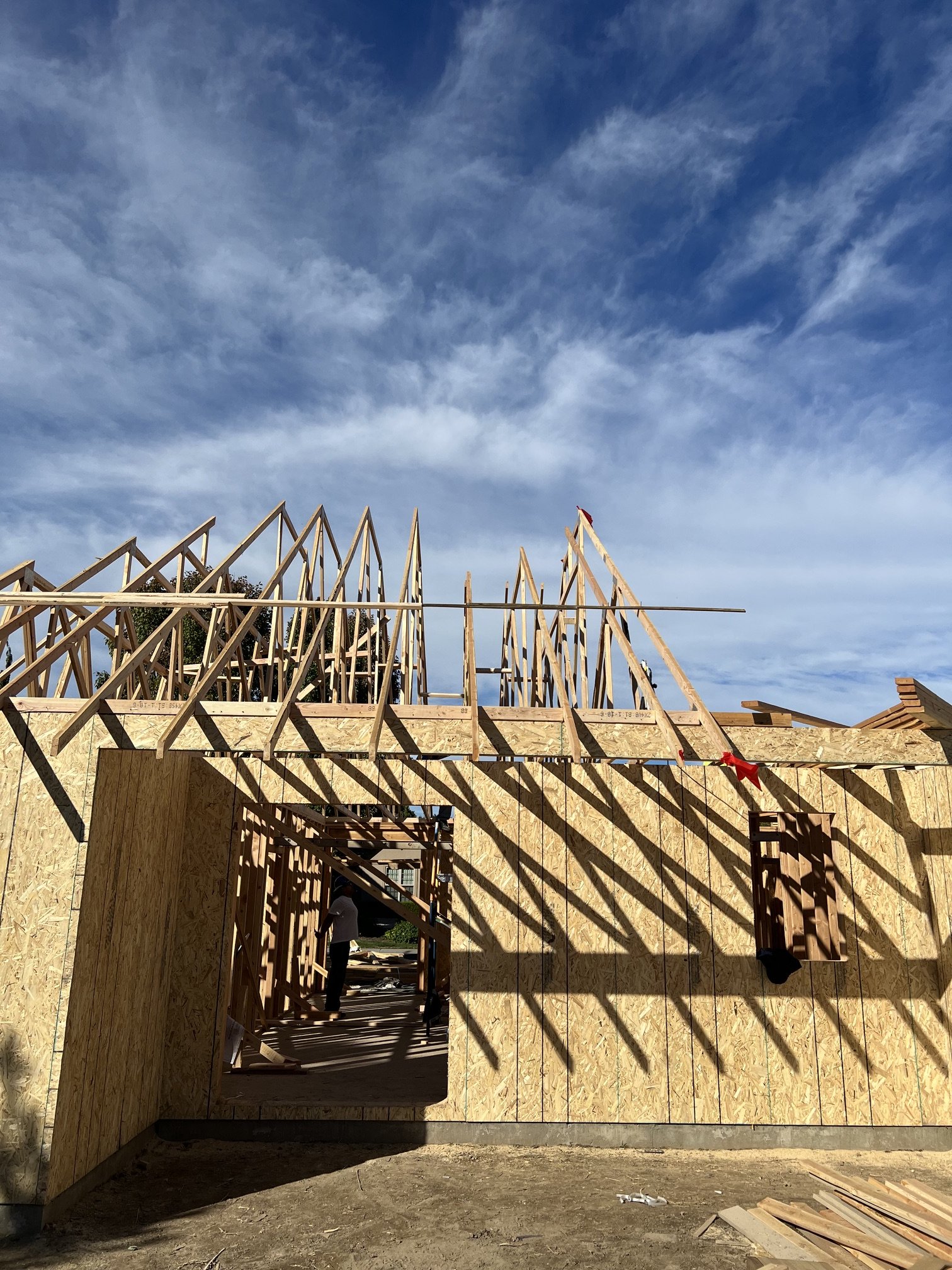 A building under construction with wooden framing and plywood walls, with a blue sky and clouds in the background.