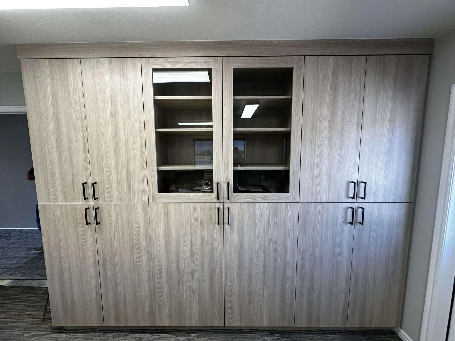 A large wooden cabinet with two glass-paneled doors in the center, flanked by solid wood doors on each side, situated against a light-colored wall with a textured ceiling.