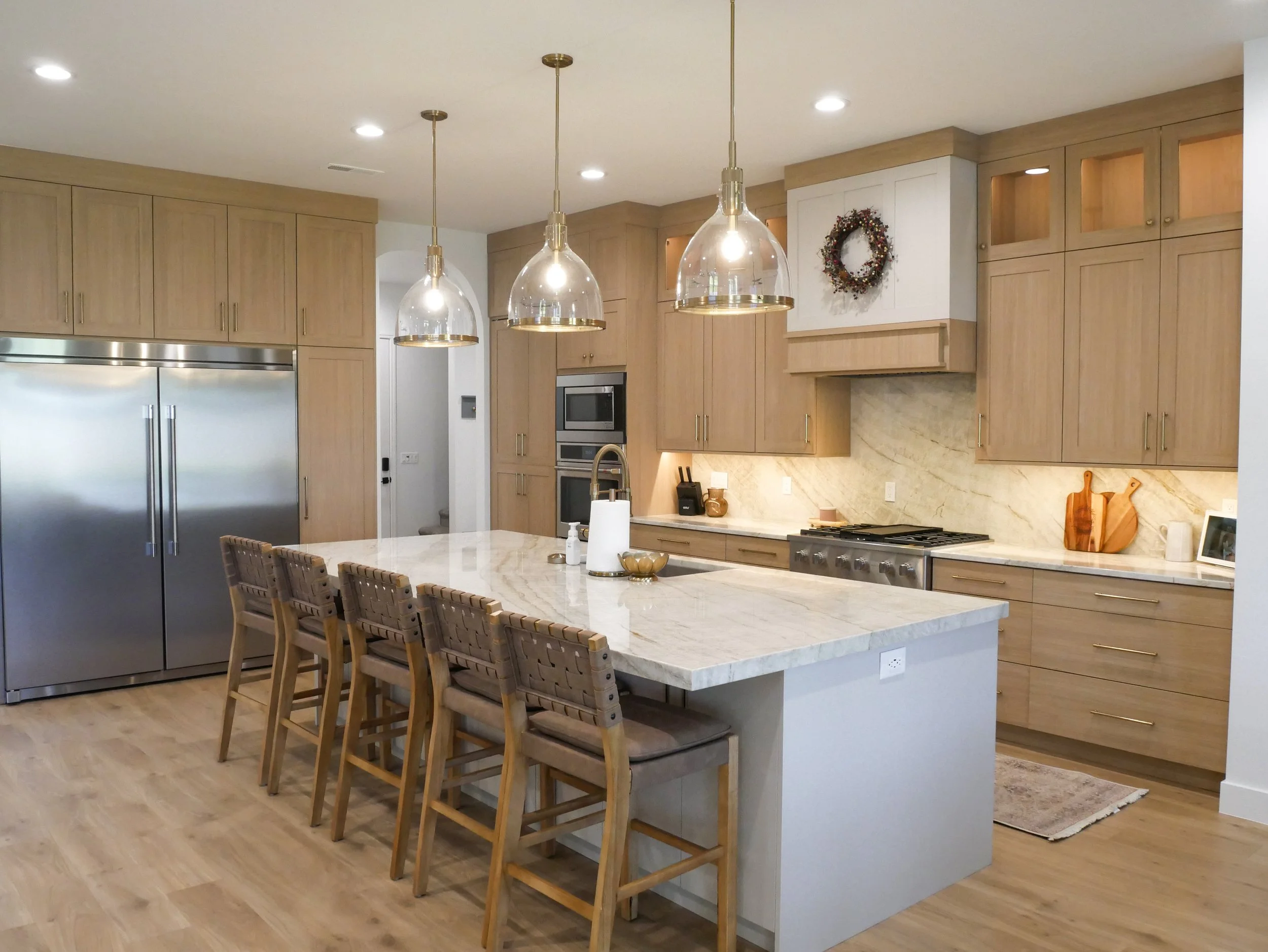 Modern kitchen with wood cabinets, stainless steel appliances, marble island, and three pendant lights.