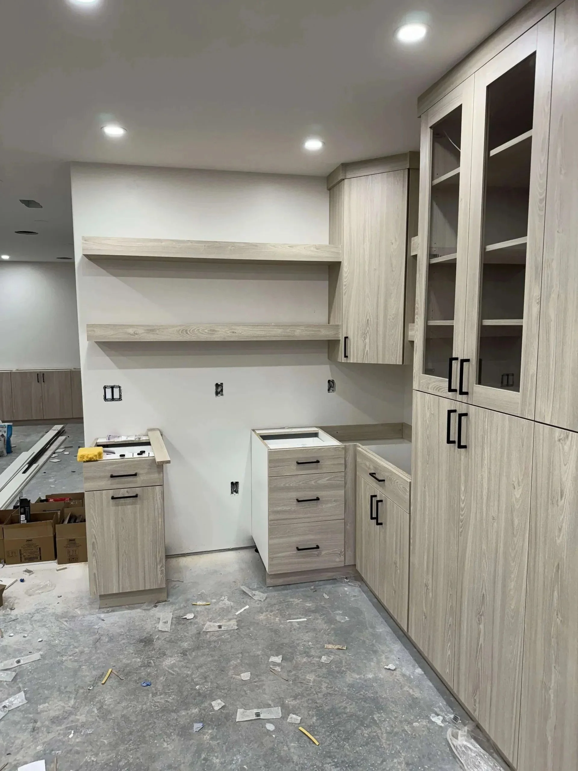 Kitchen cabinetry being installed, with unfinished drawers, scattered tools, and construction debris on the floor.