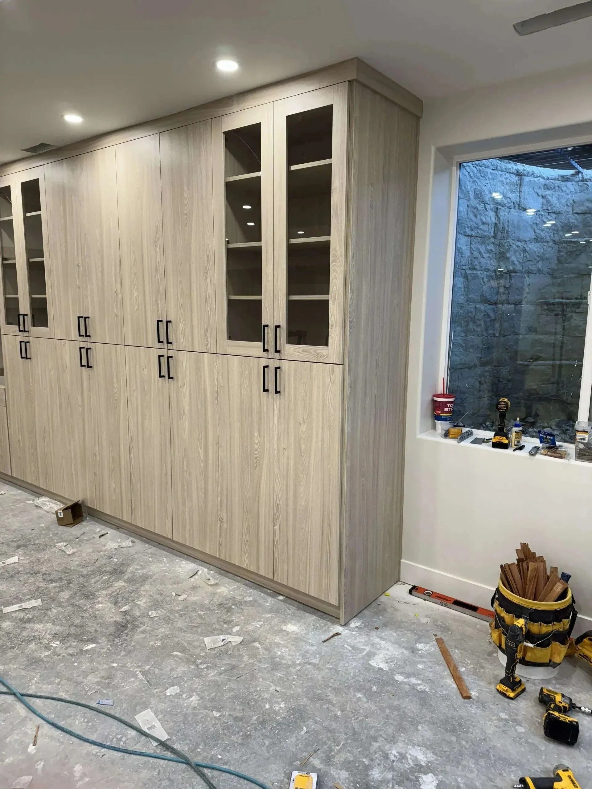 Construction site with a large built-in wooden cabinet, tools, and materials scattered on the unfinished floor.
