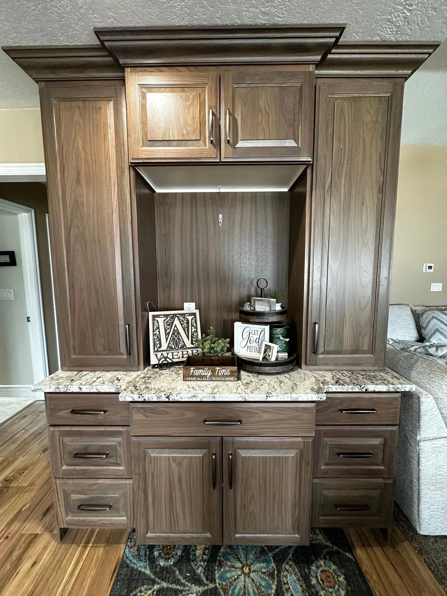 Wooden kitchen cabinets with a granite countertop and decorative items on a black round rug.