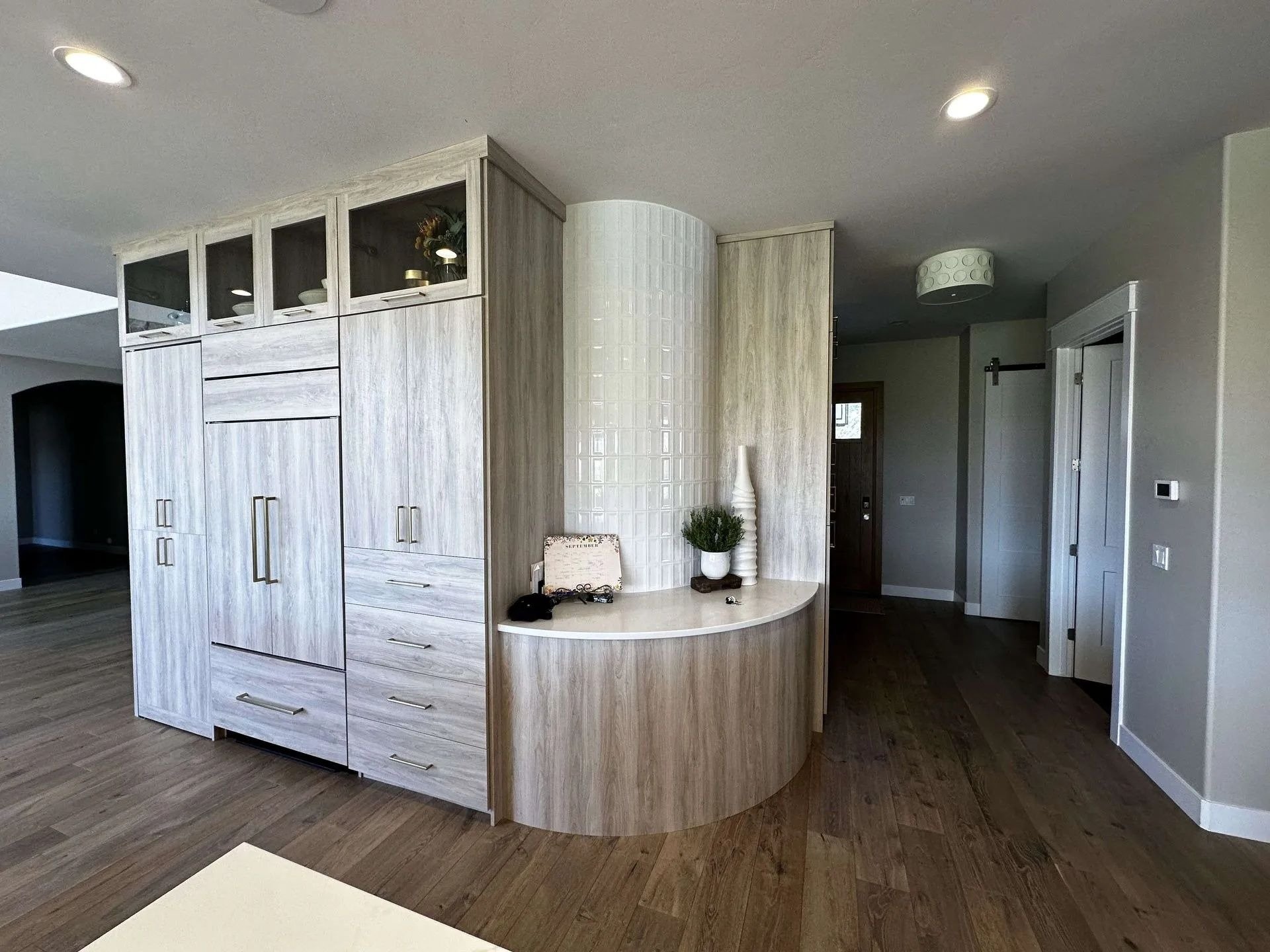 Interior of a modern home with light wood cabinetry, a curved tile accent wall, and decorative items like vases and plants on a small ledge.