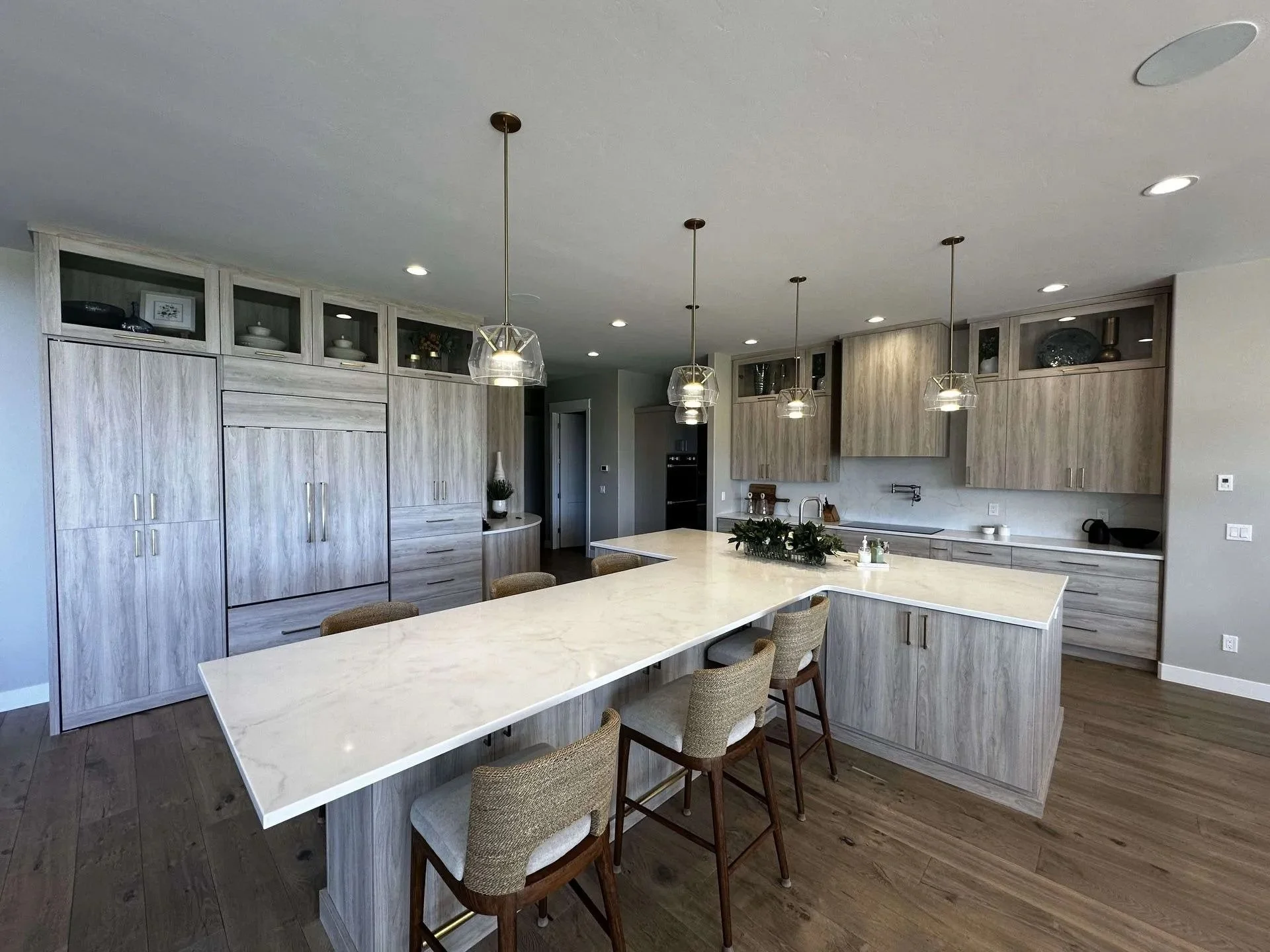 Modern kitchen with light wood cabinetry, a large white island, pendant lighting, and dark wood flooring.