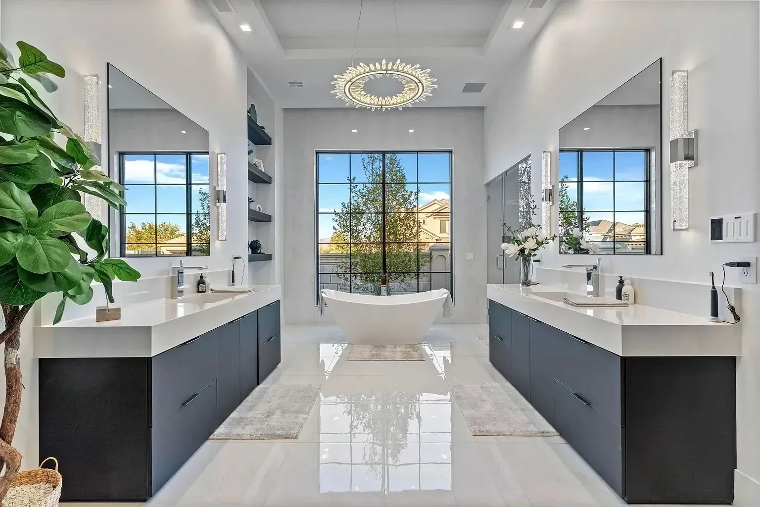Modern bathroom with dual sinks, large mirror, bathtub, large window with outdoor view, and decorative lighting.