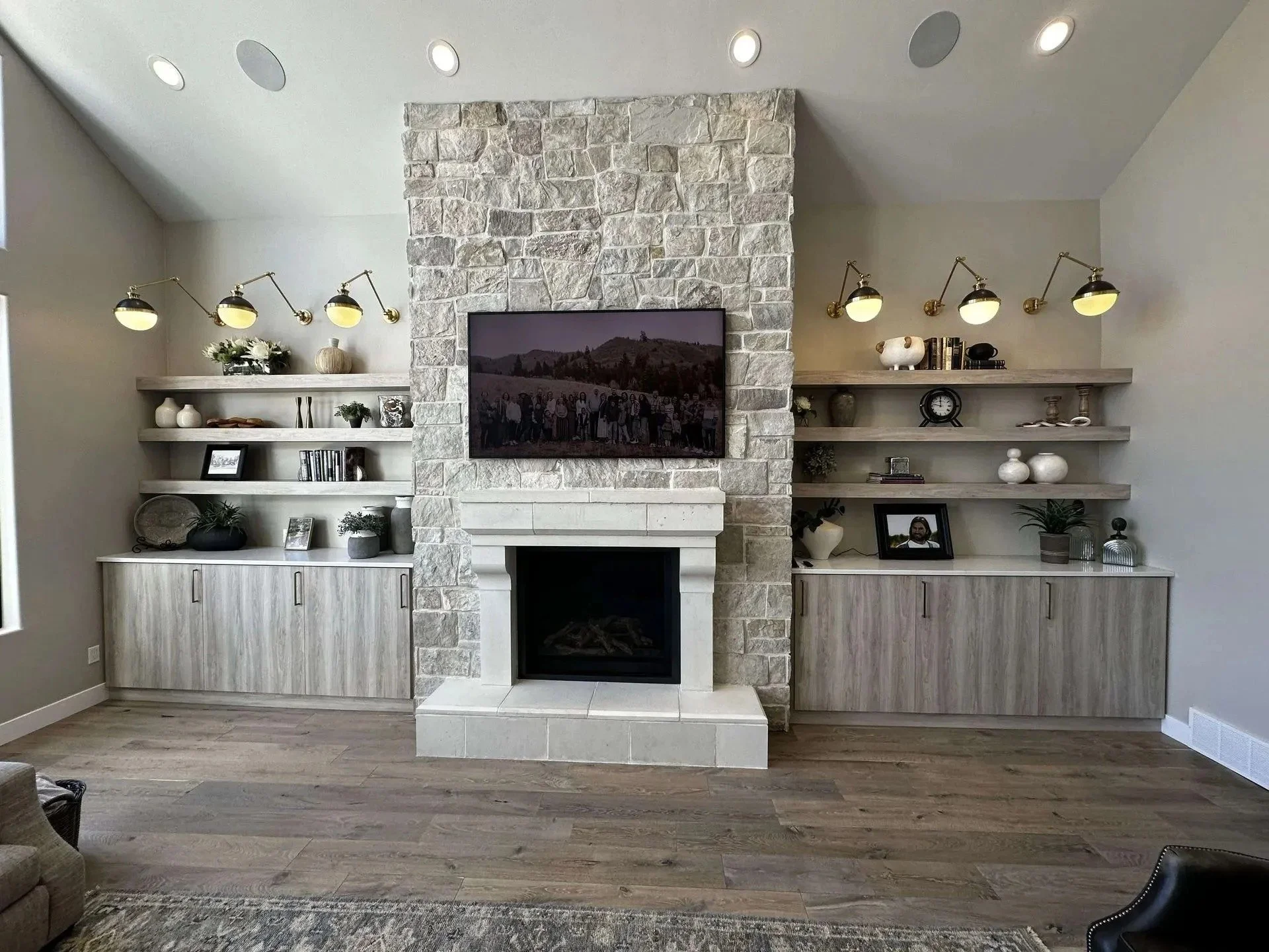 Living room featuring a stone fireplace with a mounted television, surrounded by built-in shelves with decorative items, artwork, and books.