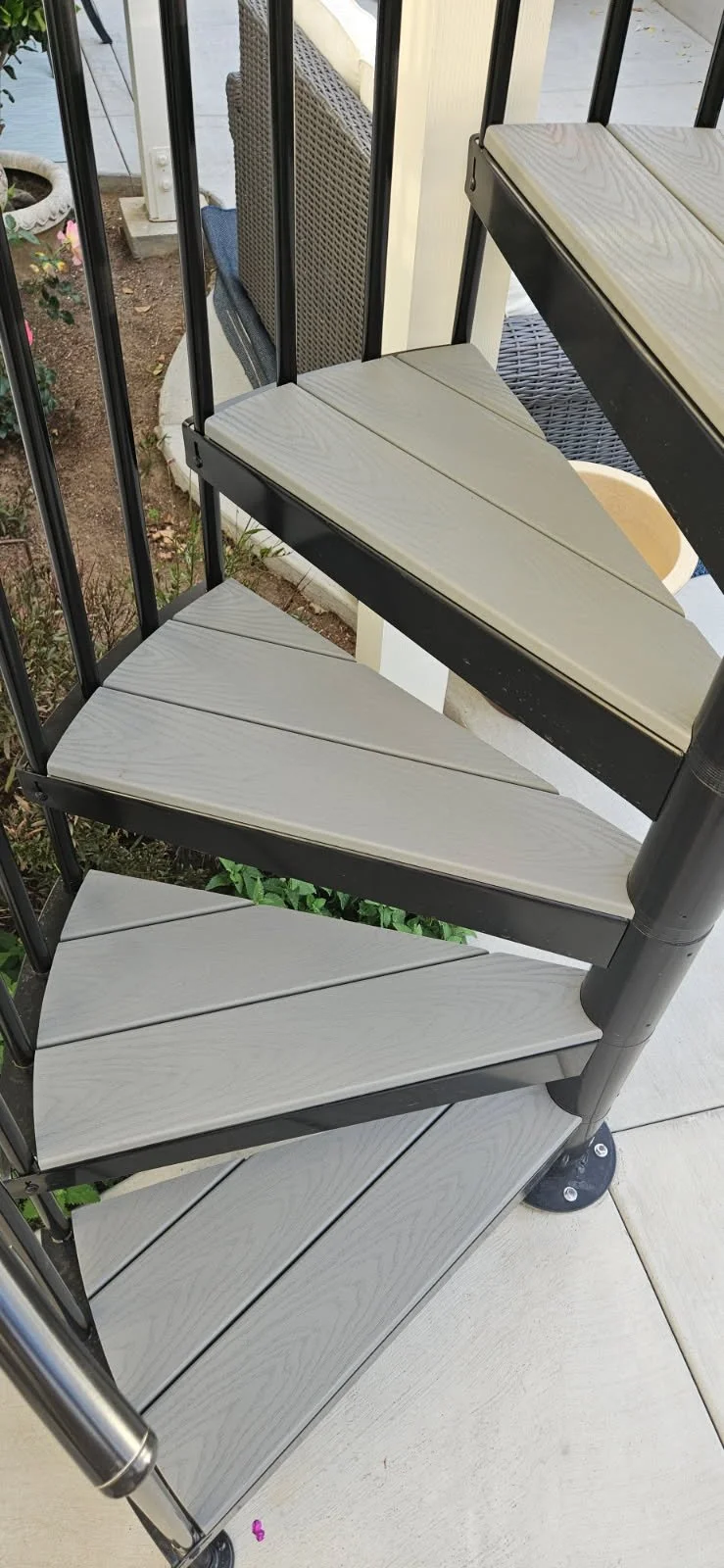 A spiral staircase with light gray wooden steps and black metal railings outside on a porch.
