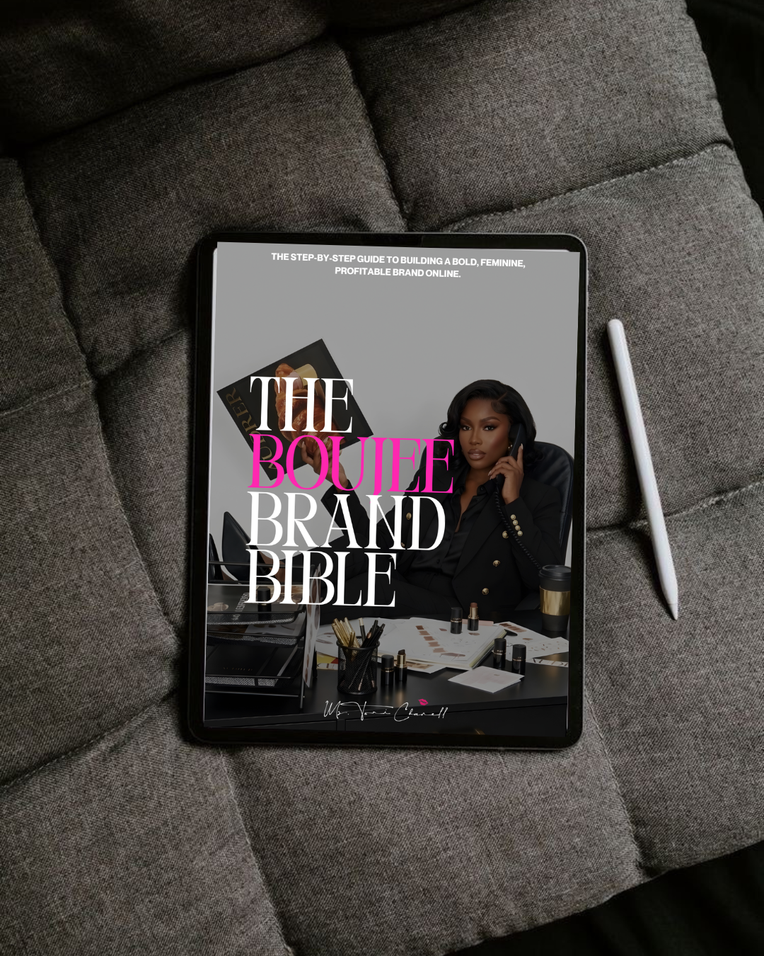 An iPad displaying a book cover titled "The Boujee Brand Bible" resting on a gray fabric couch with a white stylus pen beside it.