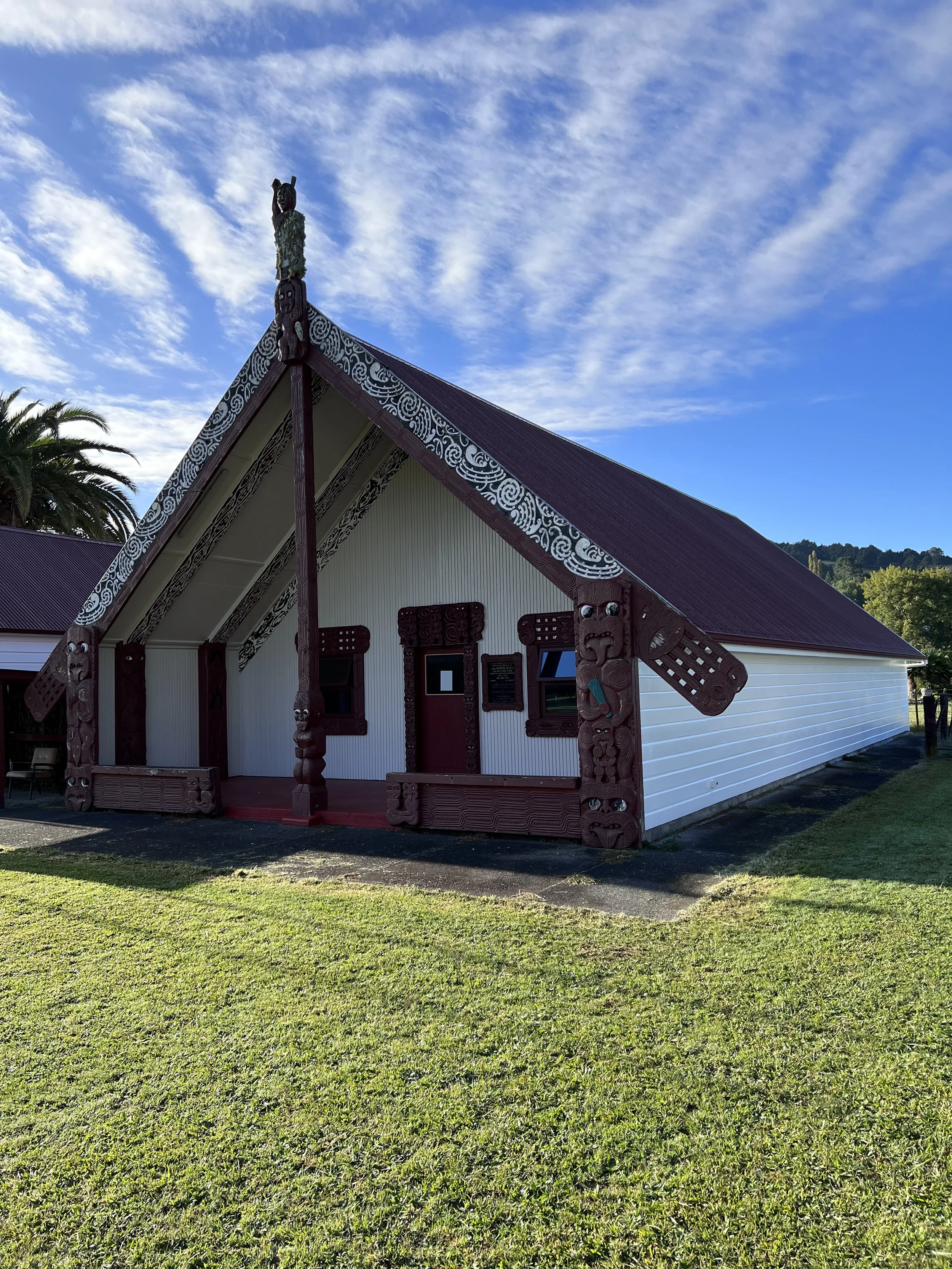 A traditional Polynesian church with intricate carvings and a statue on the roof, surrounded by green lawn and a bright blue sky with clouds.