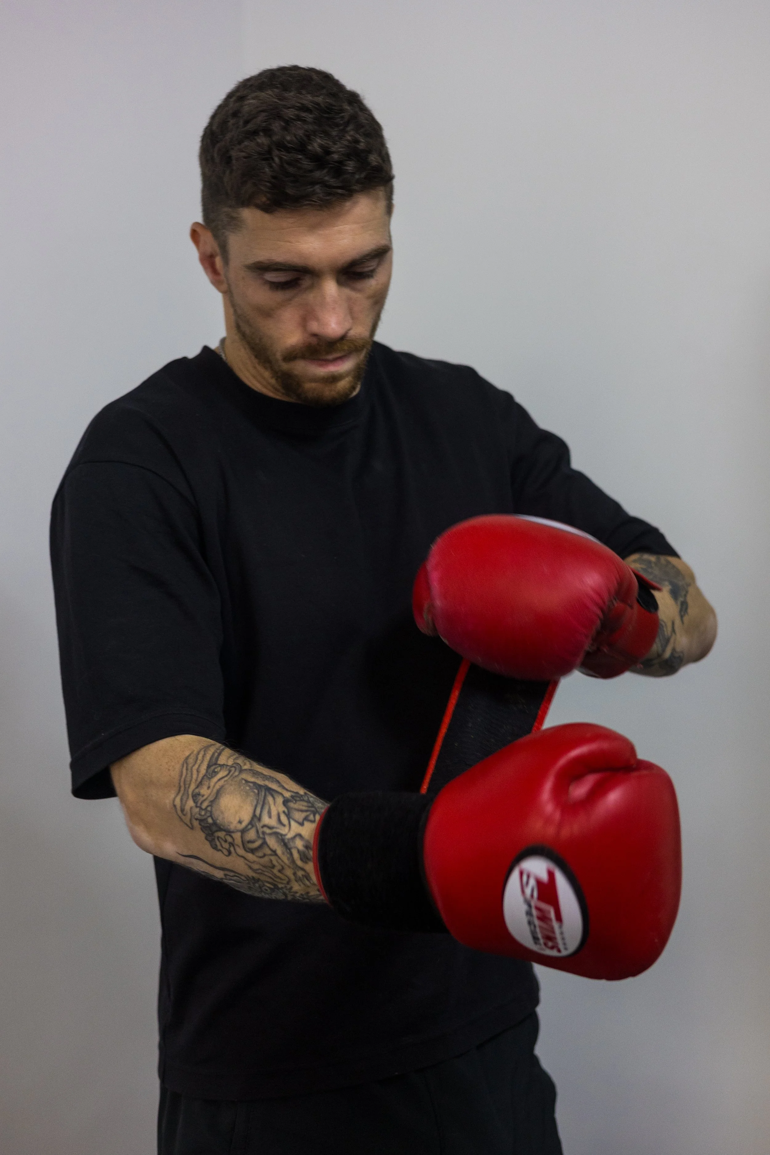 Un coach qui enfile et attache ses gants de boxe face à un mur blanc.