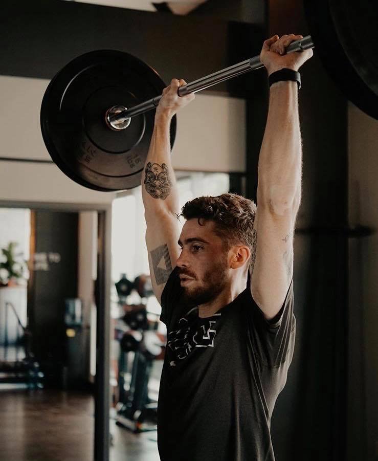 Un homme soulève une barre avec un poids au-dessus de sa tête dans une salle de sport.