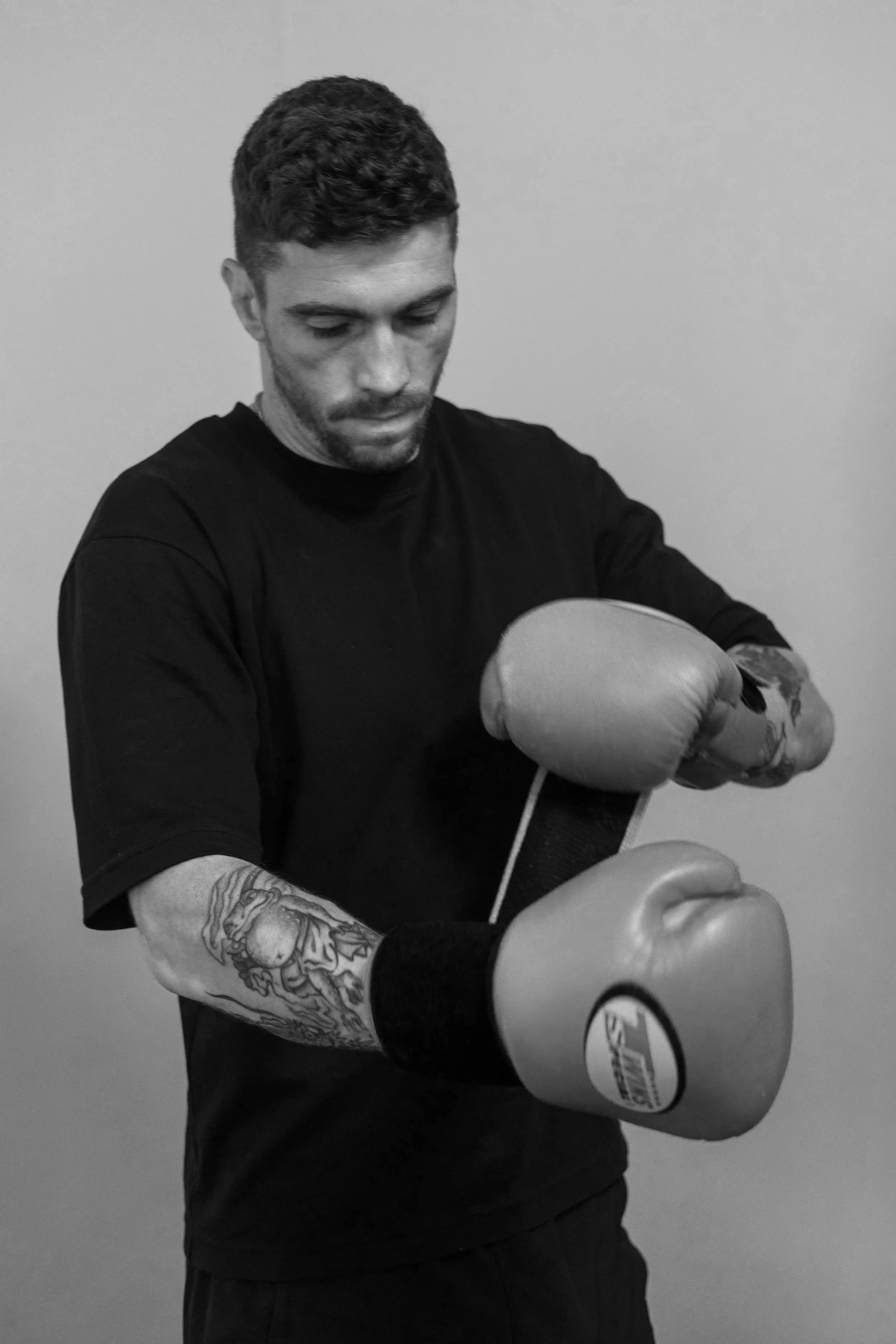 Un homme portant des gants de boxe noir, en train de s'entraîner ou de se préparer à boxer, sur un fond gris clair.