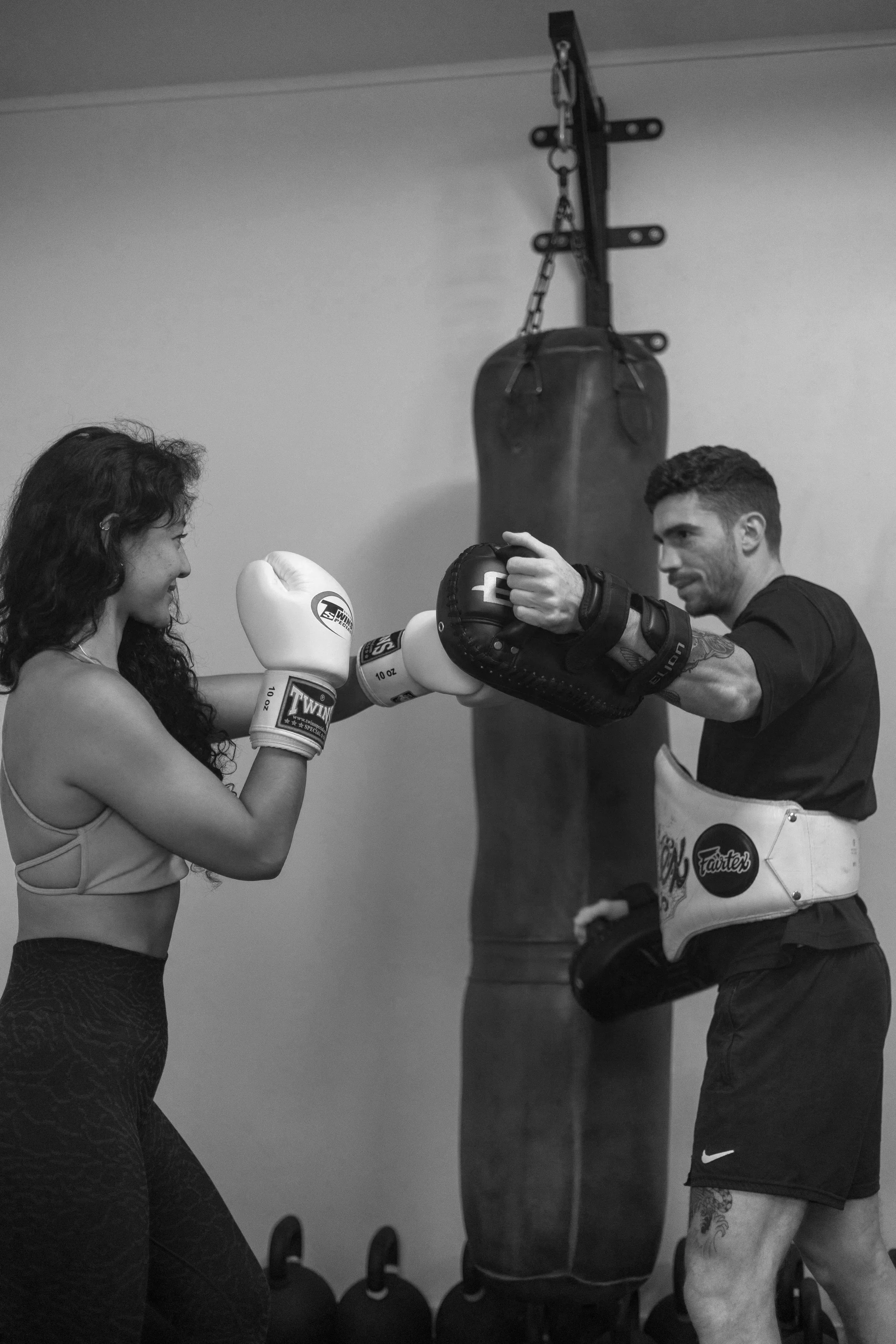 Une femme et un homme s'entraînent dans une salle de sport, ils portent des gants de boxe pratique ou s'entraîne en boxe, avec un sac de boxe suspendu au mur en arrière-plan.