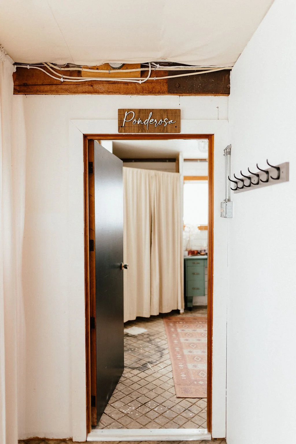 Doorway with a sign that reads 'Ponderosa' above it, leading into a room with a beige curtain, a green dresser, and a patterned rug on the floor.