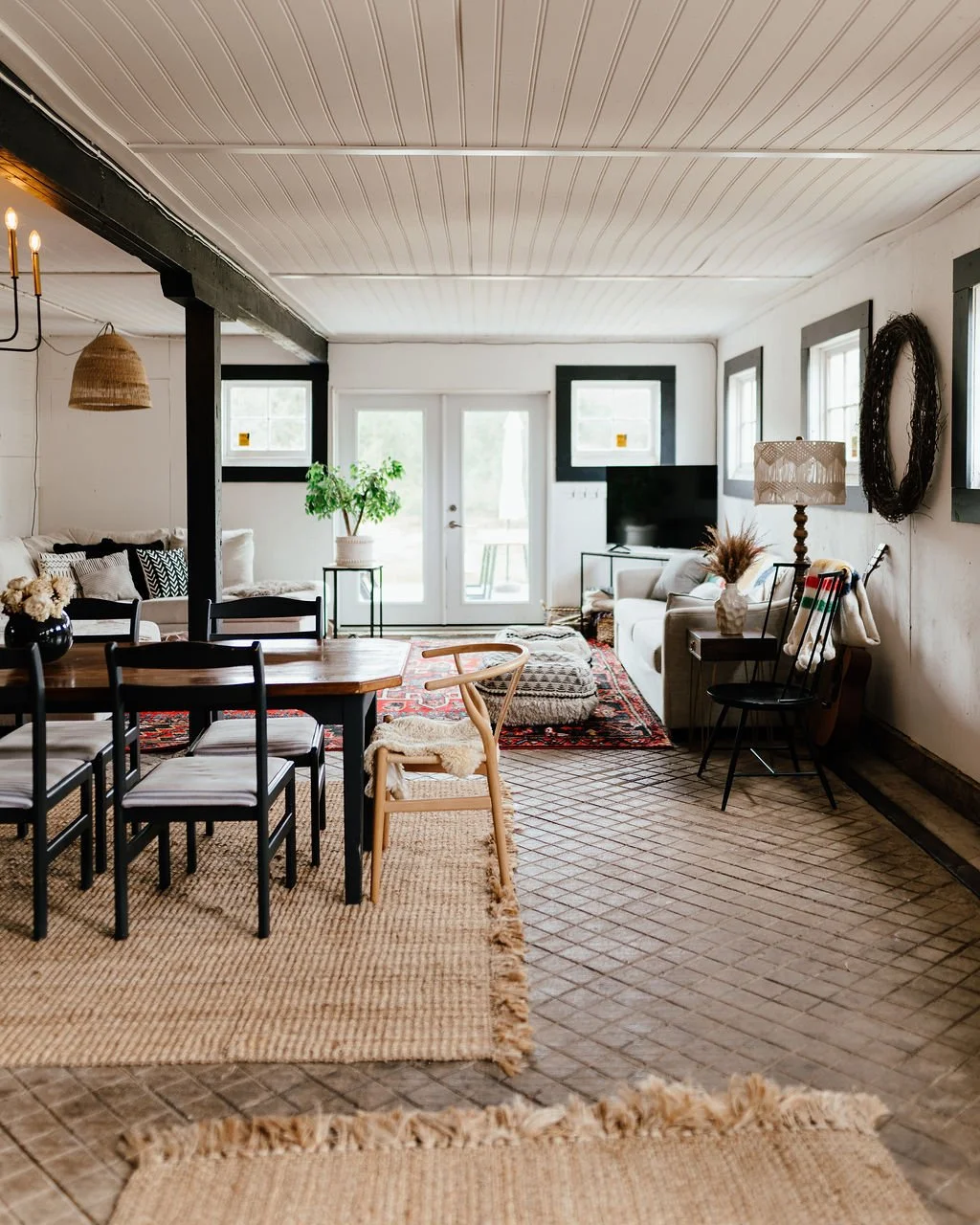 Living room and dining area with black dining table, chairs, white couches, patterned rug, and decorative items.
