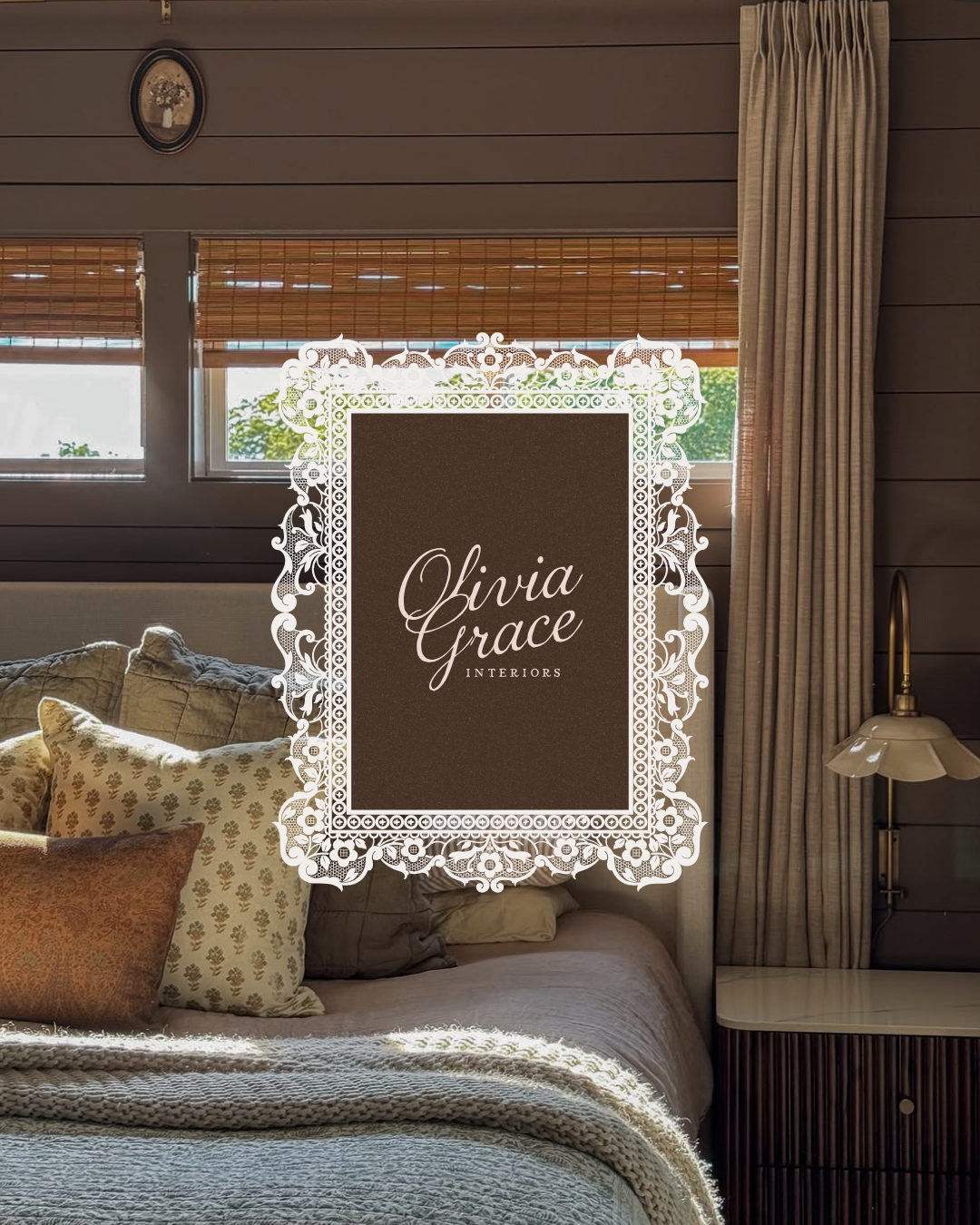 A cozy bedroom scene with a bed filled with pillows, a textured blanket, and soft sunlight coming through the window. The room features wood-paneled walls, window blinds, and beige curtains. There is a nightstand with a lamp on the right side. Overlaid in the center is a decorative lace frame with the text "Olivia Grace Interiors".