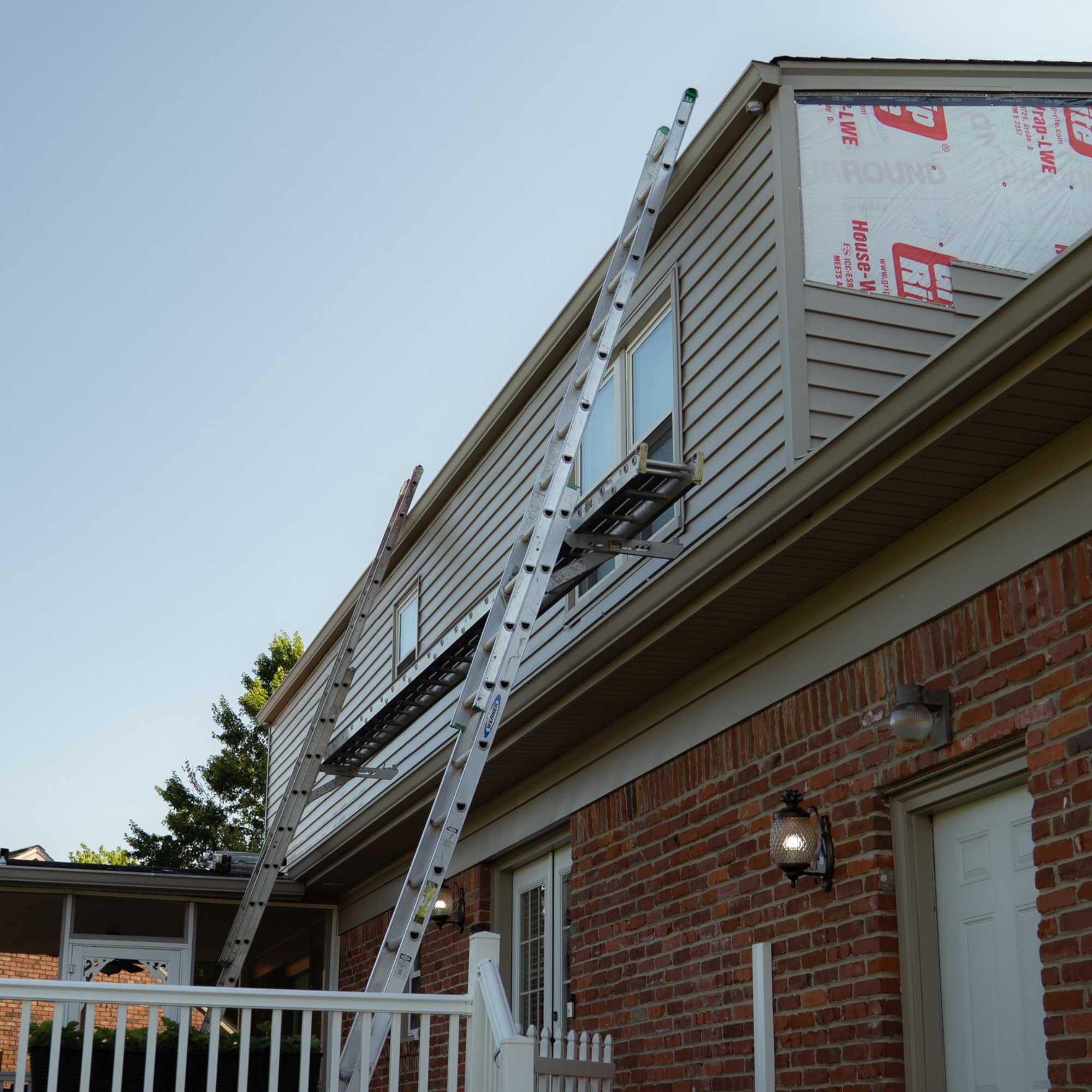 Ladder leaning against the side of a house under construction or renovation, with a brick exterior and a partially installed window