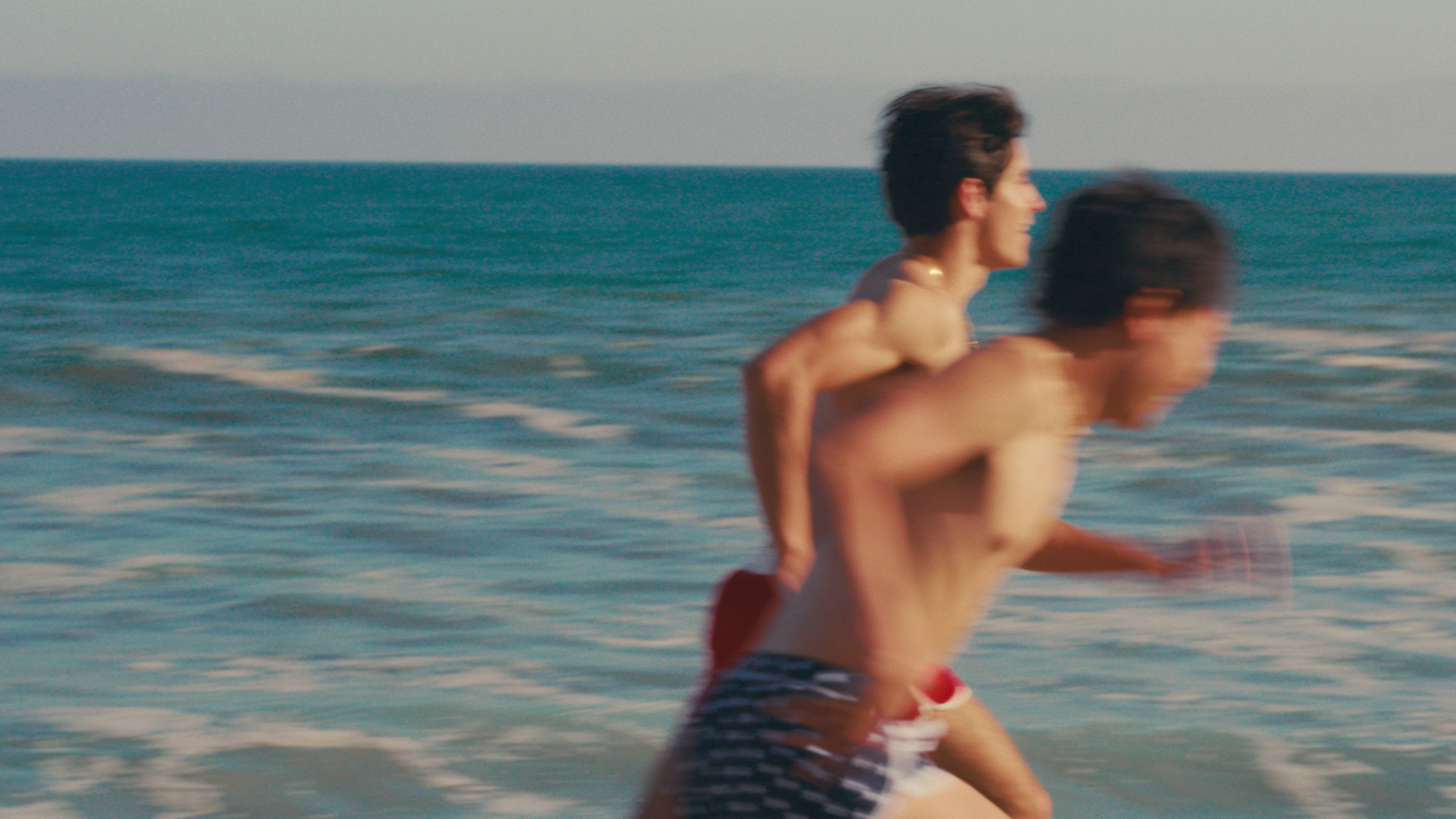 Two young men running along the shoreline at the beach with the ocean in the background