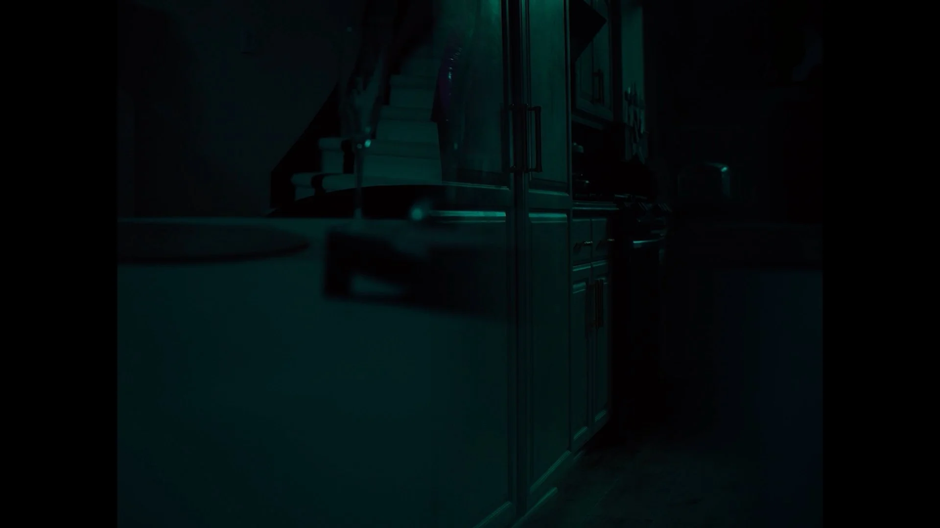 Dimly lit kitchen with dark wooden cabinets, a countertop, and a white stove, illuminated by faint greenish light.