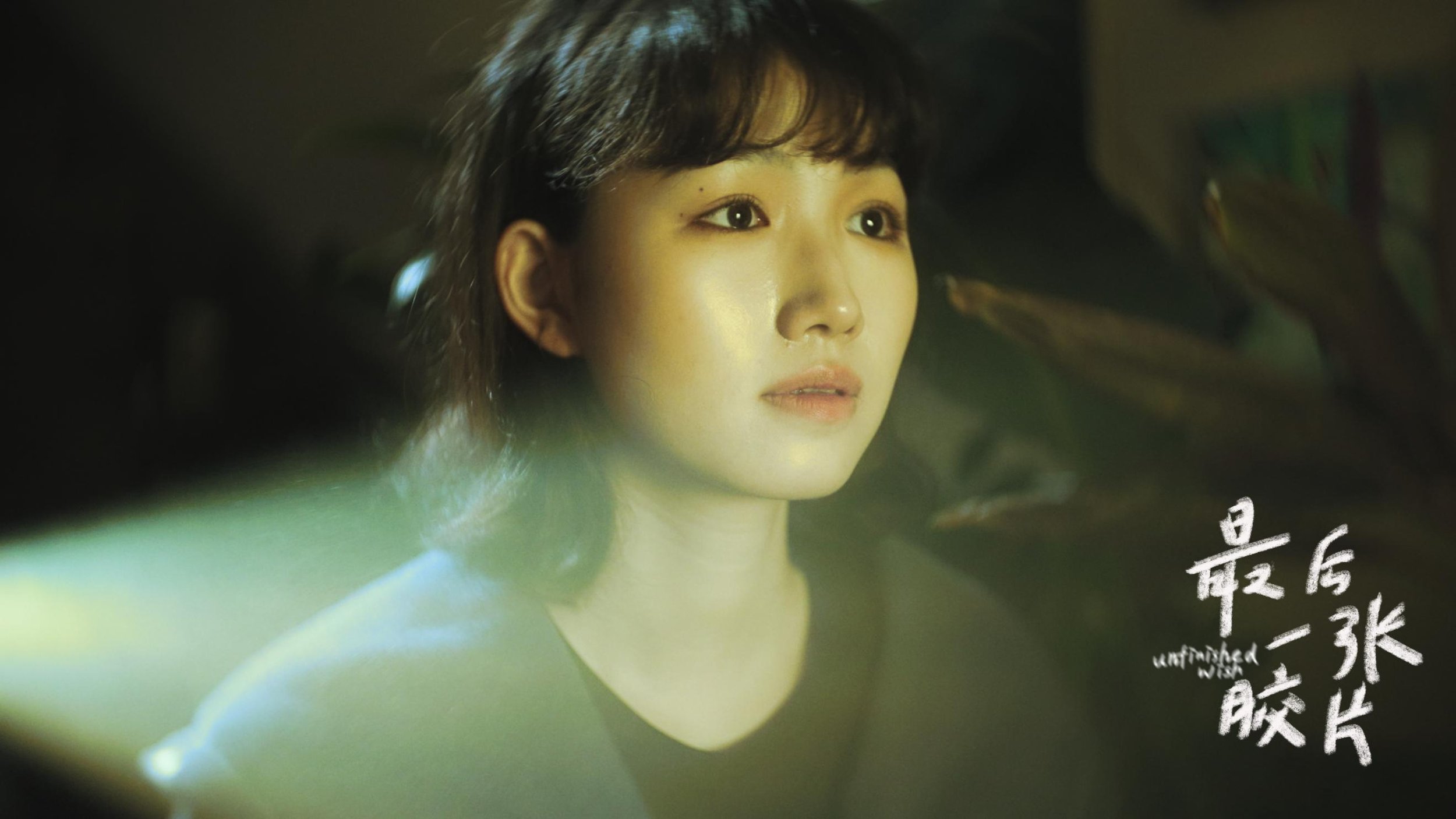 Close-up of a young woman's face with dark hair and expressive eyes, against a dark background with Chinese characters written in white.