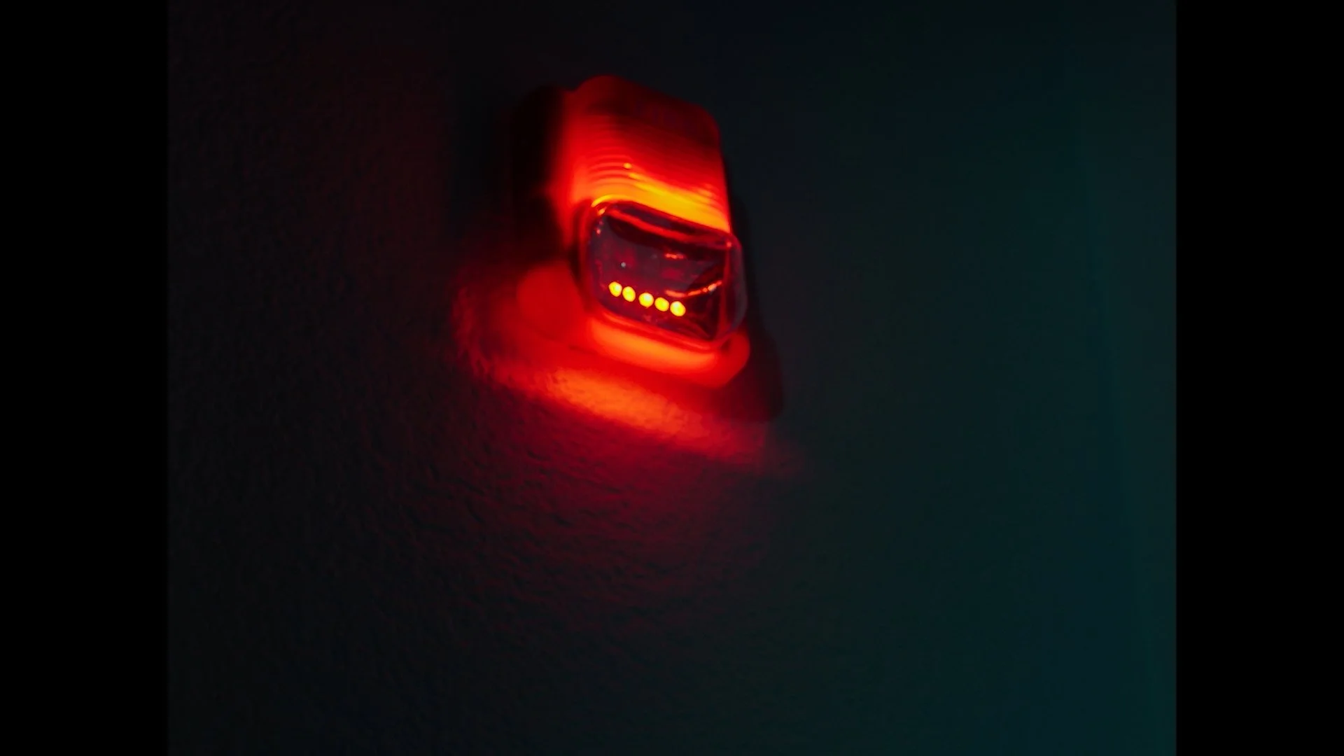 Red LED light illuminated on a dark wall, indicating an electronic device is active or powered on.