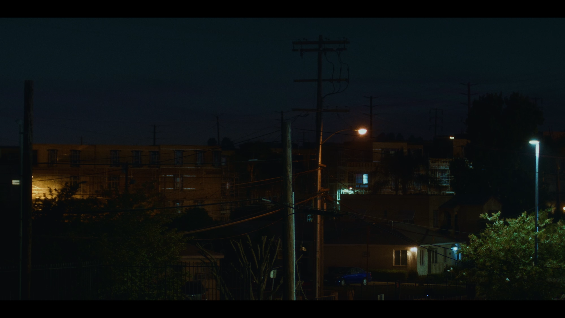 Nighttime urban scene with streetlights, power lines, and buildings in the distance under a dark sky.