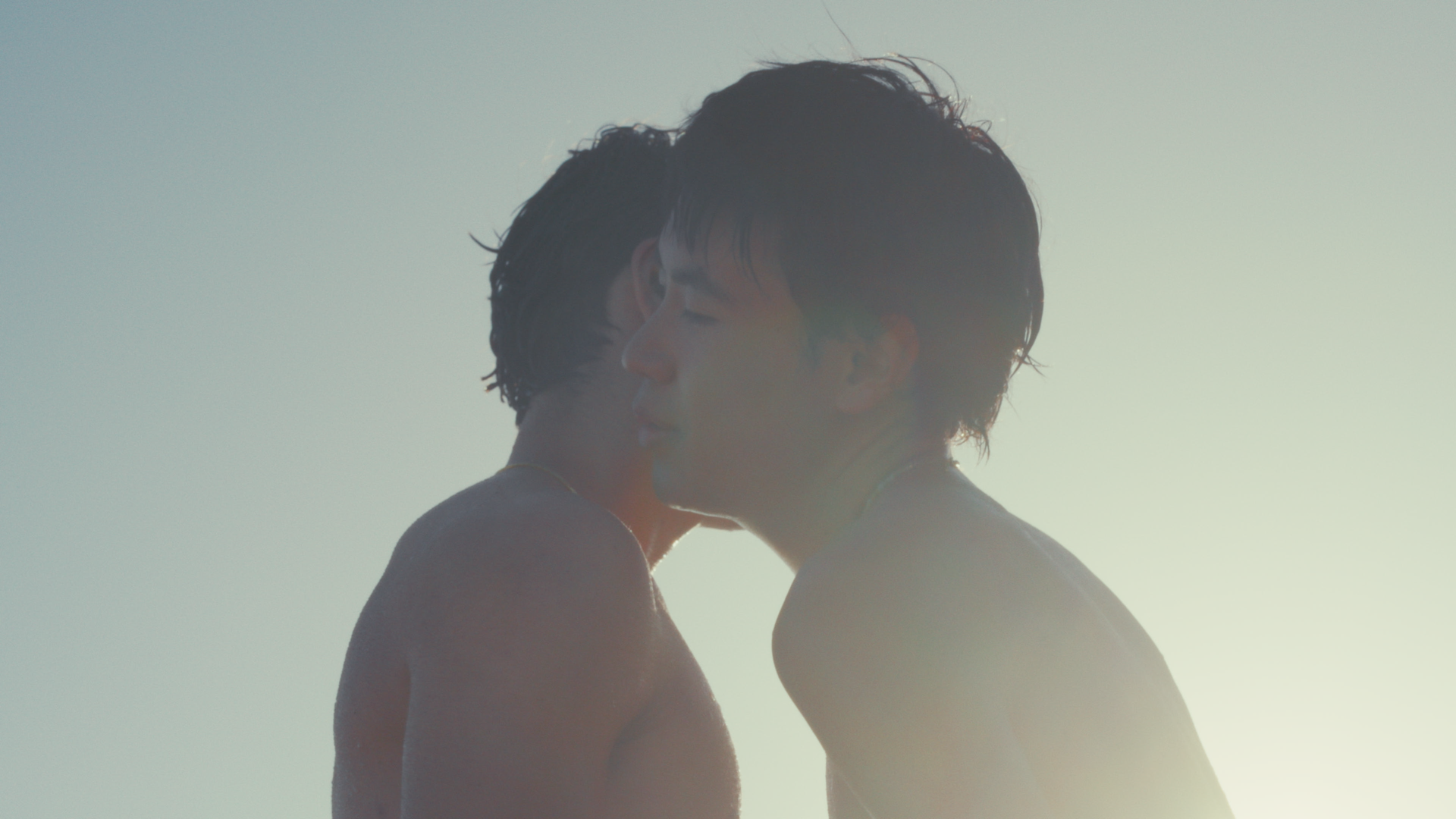 Two people are close together, sharing a kiss, with a bright, softly lit background.