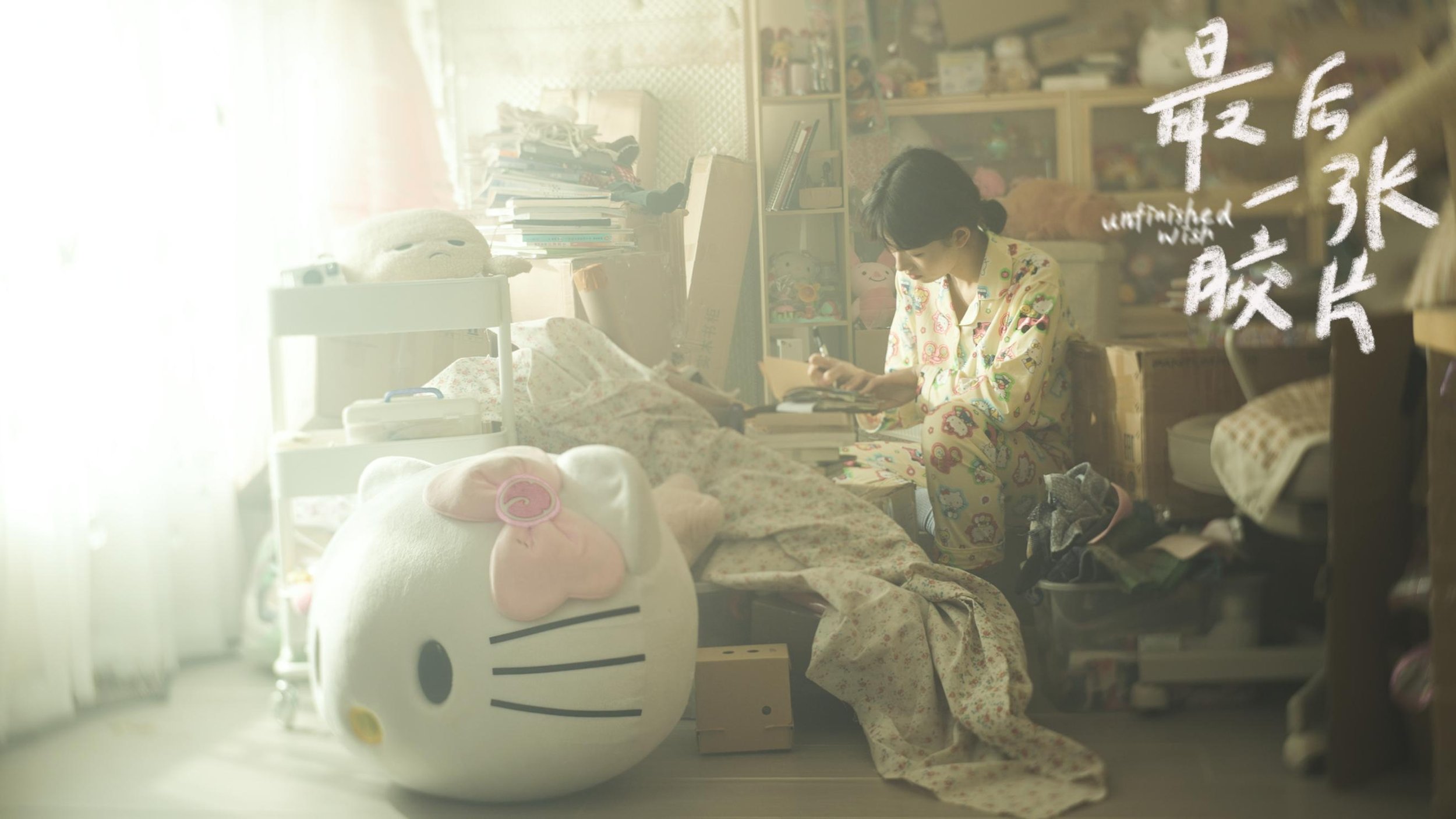 A woman in pajama pants and a pajama top kneeling beside a hospital bed, writing in a notebook. The bed has a stuffed pig toy and various medical equipment. The room is cluttered with books and toys.