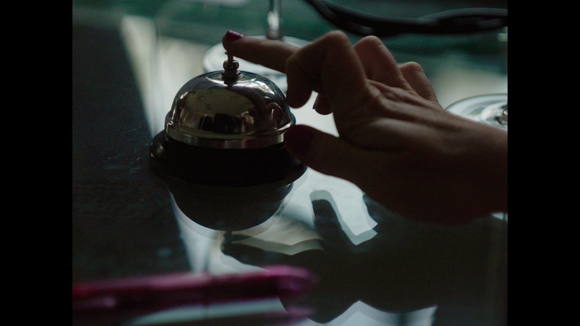Close-up of a person's hand pressing a button on a small, shiny, metallic device on a dark surface, with the reflection visible.