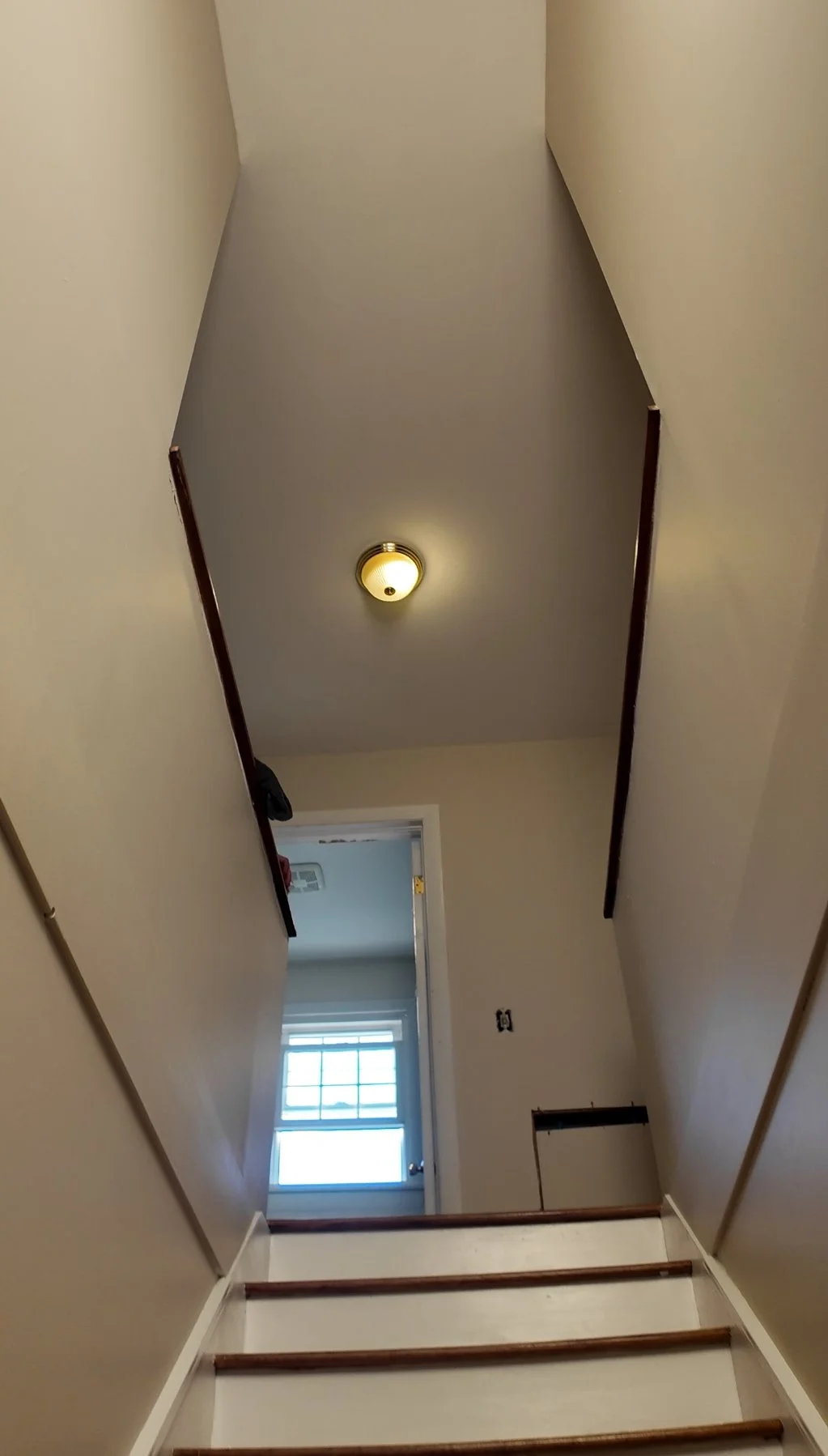 Interior view of a stairwell leading to a doorway with a window, ceiling light fixture, and beige walls.
